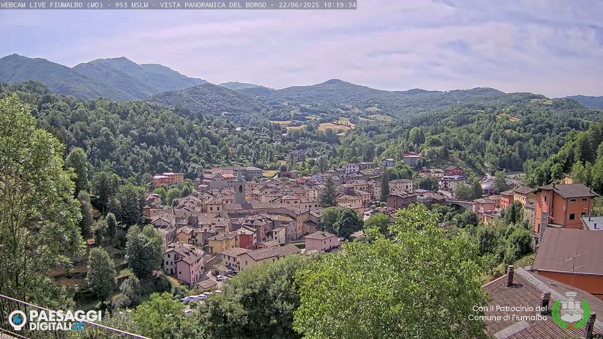 A picturesque village nestled in a valley surrounded by verdant hills and mountains under a partly cloudy sky.