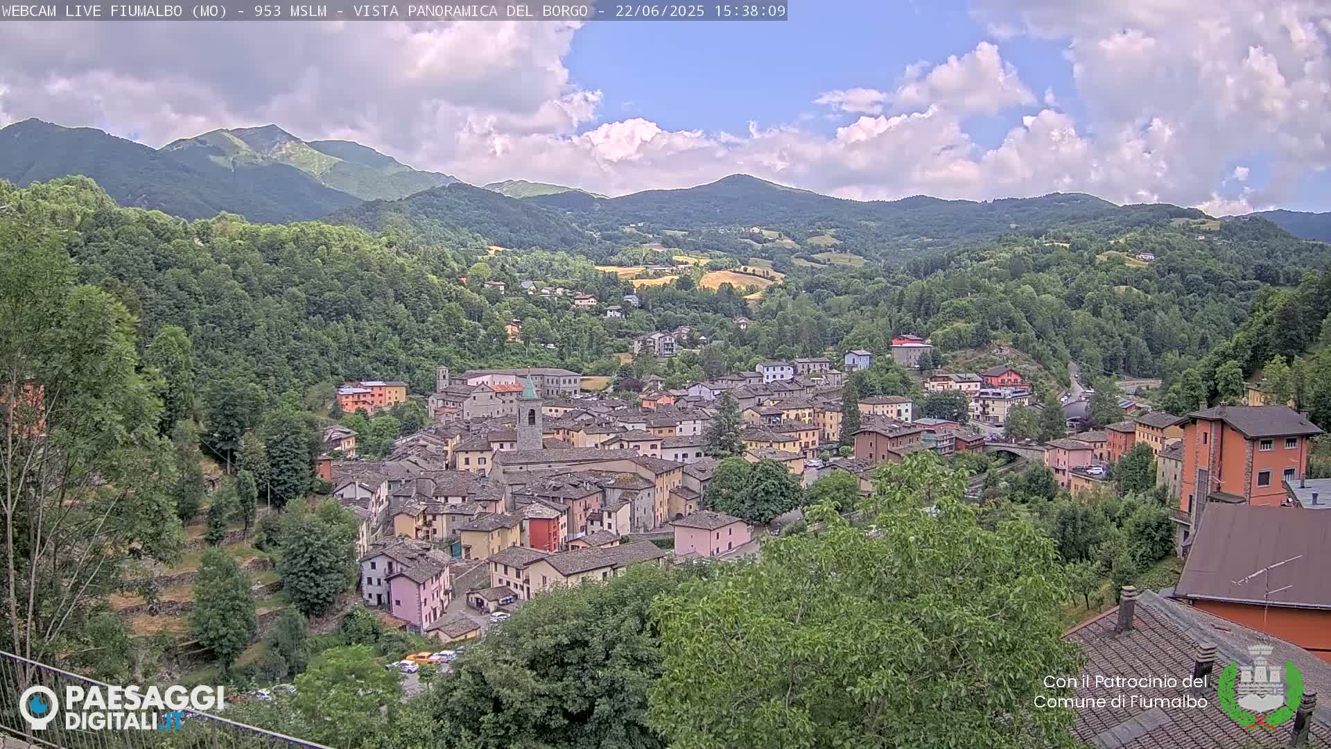 A picturesque village nestled in a valley surrounded by lush green hills and mountains under a partly cloudy sky.