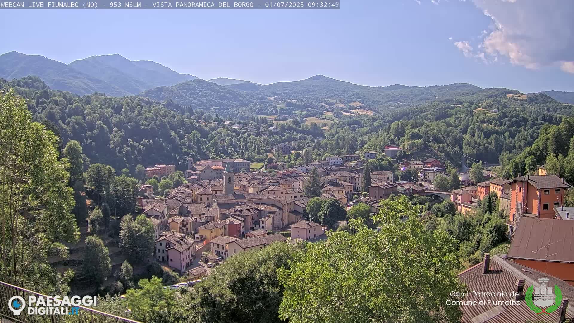 A small town nestled in a valley surrounded by lush green hills and mountains under a mostly clear sky.