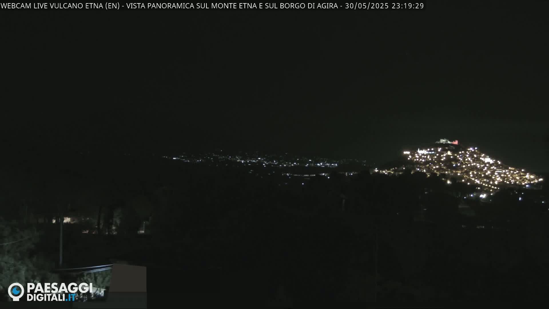 A nighttime long shot shows a hilltop town illuminated by many lights against a dark, clear sky.