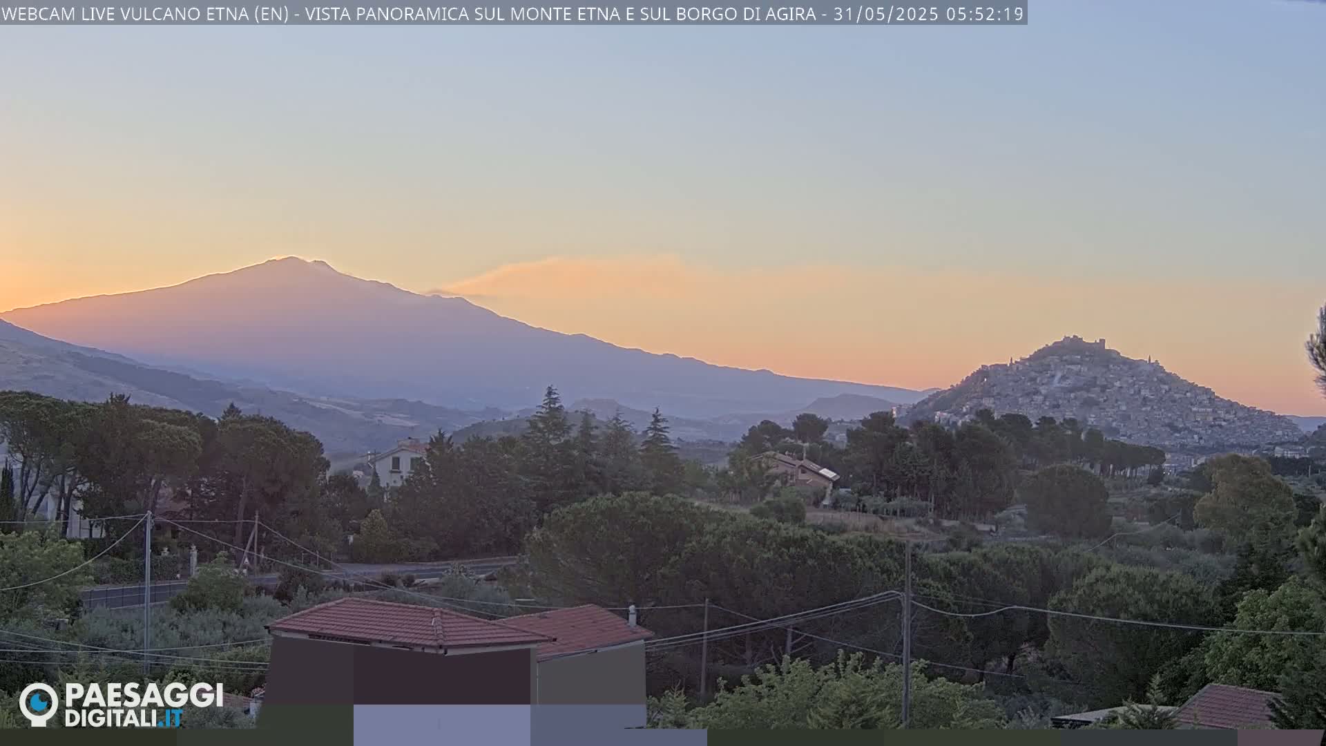 A sunset view shows Mount Etna in the distance, with a town nestled on a hill in the foreground, under a clear sky.