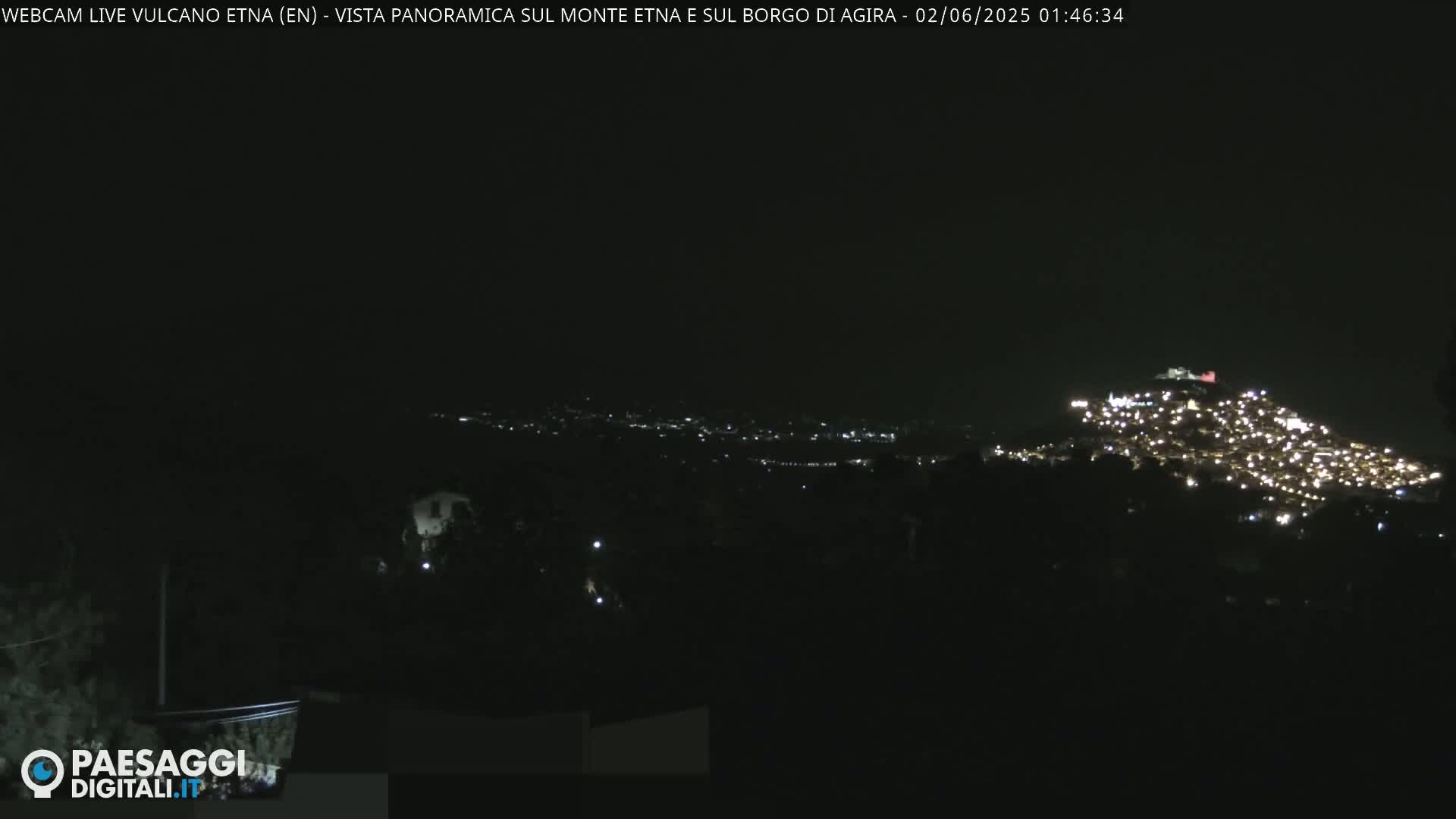 A nighttime, long shot shows a hilltop town illuminated by lights against a dark sky.