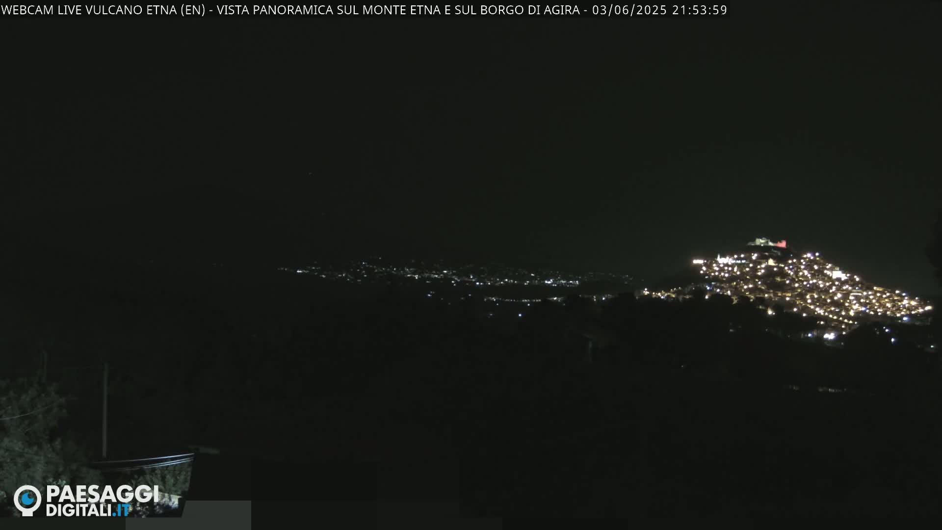 A nighttime, long-distance view shows a hilltop town illuminated by many lights against a dark sky.