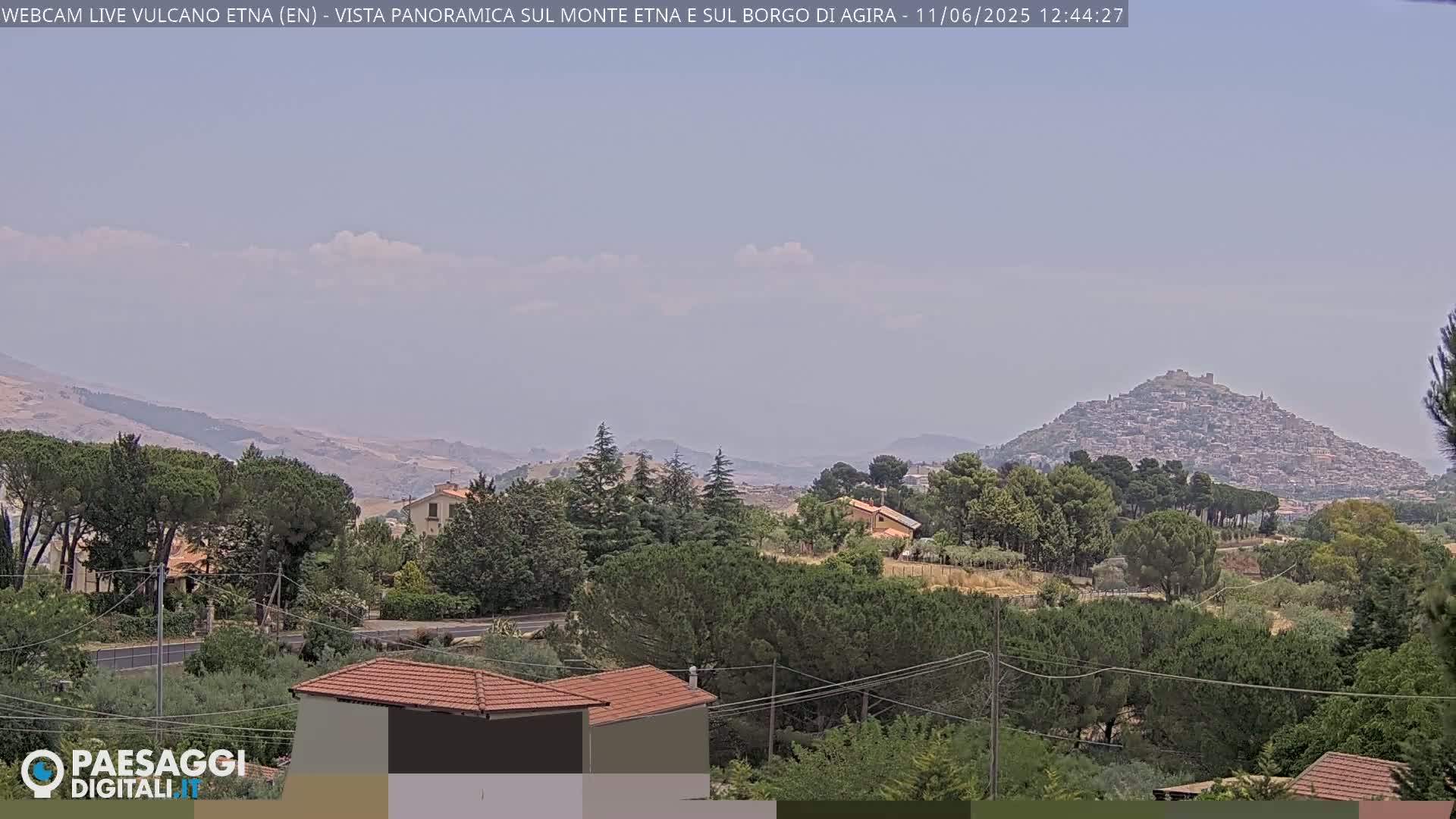 A hazy, distant view of a hilltop town nestled among rolling hills and lush green trees.