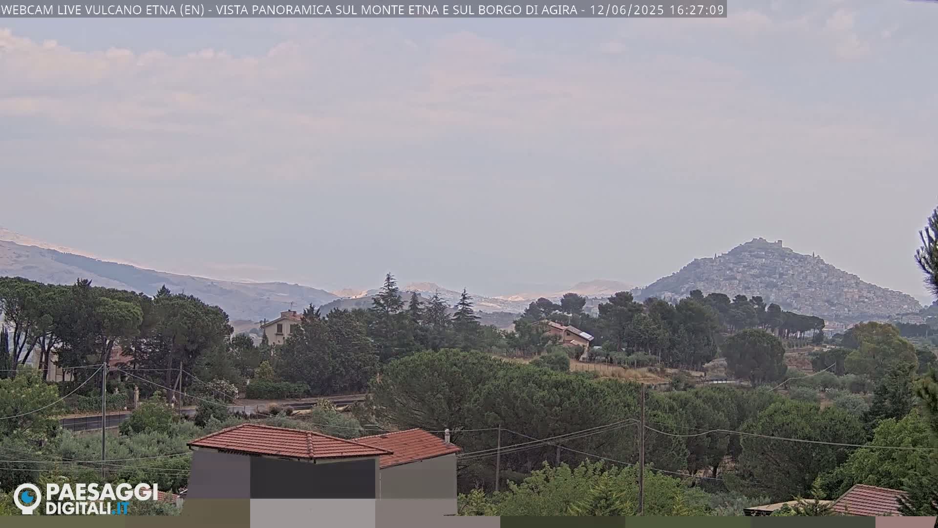A hazy, overcast day reveals a distant hilltop town nestled among rolling hills and green vegetation, with more mountains visible in the far background.