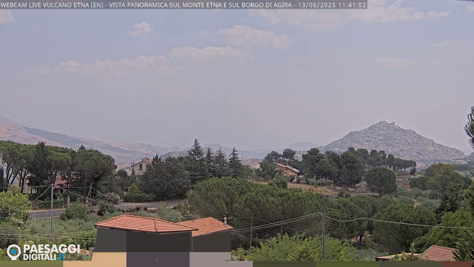 A hazy, partly cloudy day reveals a distant hilltop town nestled among green trees and rolling hills.