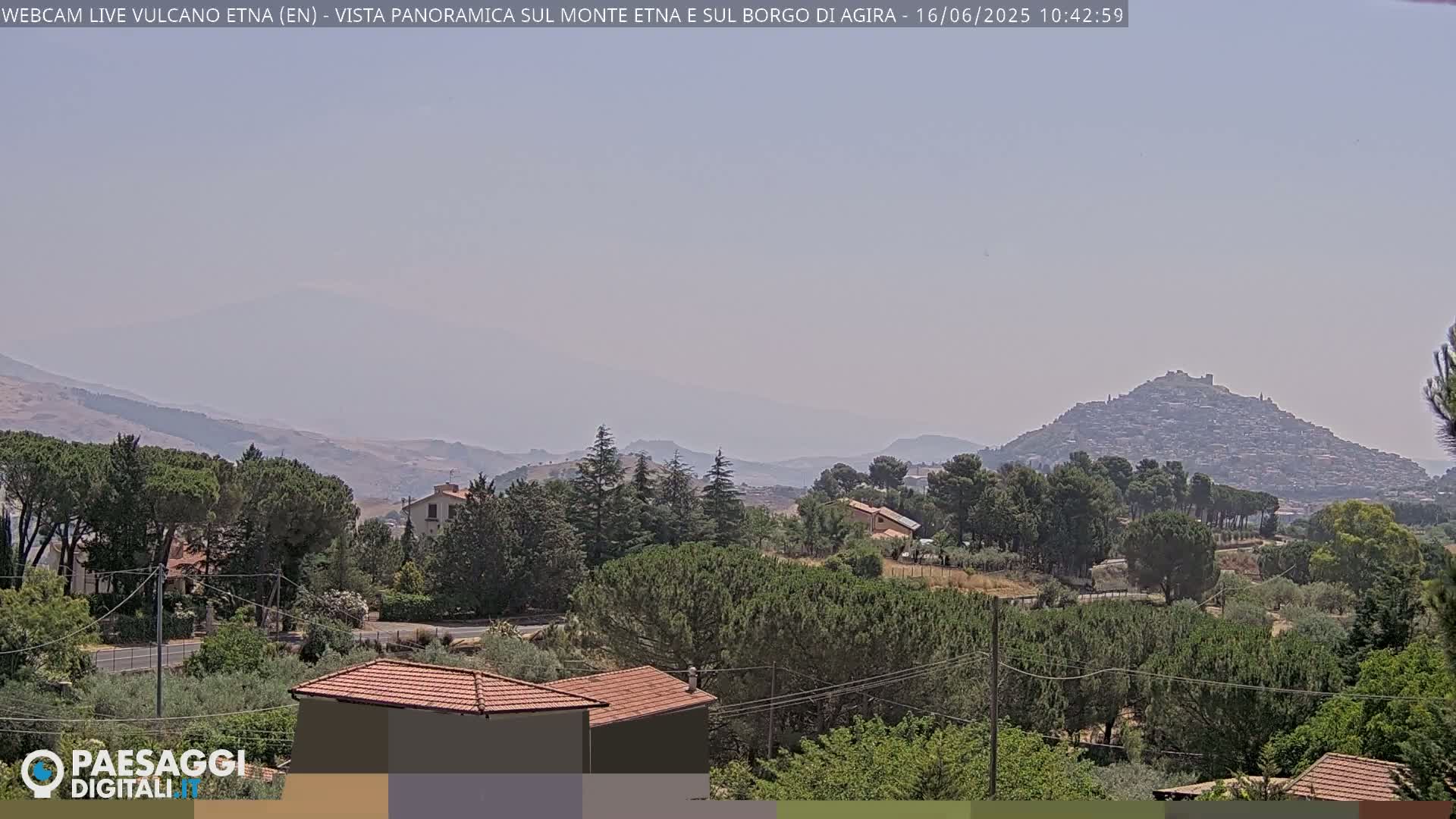 A hazy, distant view of a hilltop town nestled among green hills and trees under a pale sky.