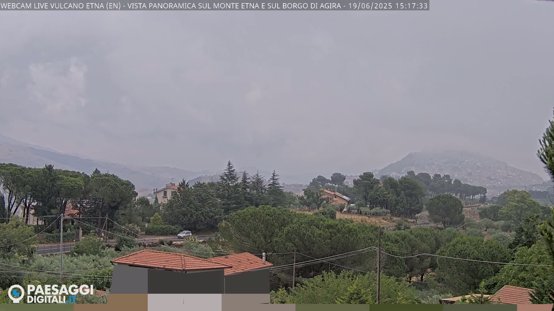 A hazy, overcast view shows a tree-covered landscape with houses and a distant, hazy mountain range.
