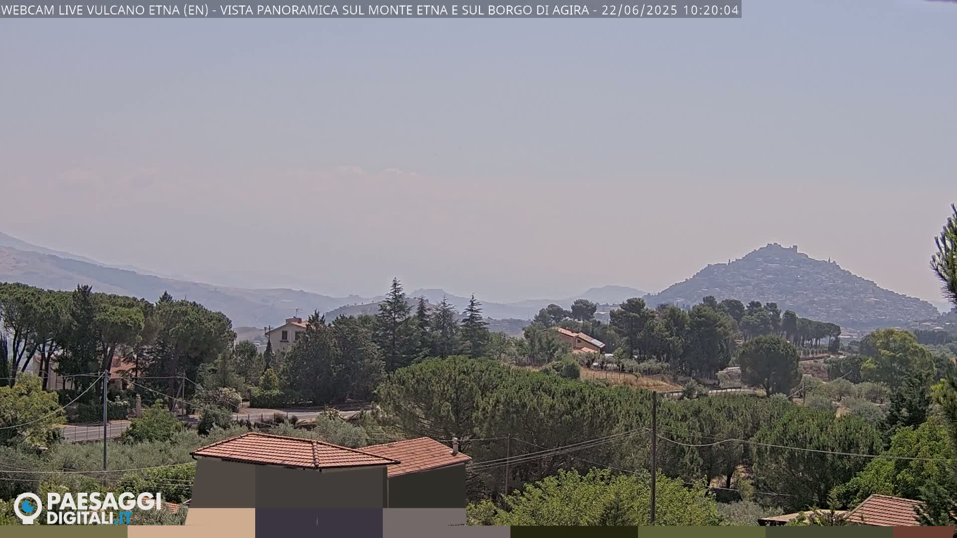 A hazy, sunny day reveals a panoramic view of a hilltop town nestled among green trees and rolling hills.