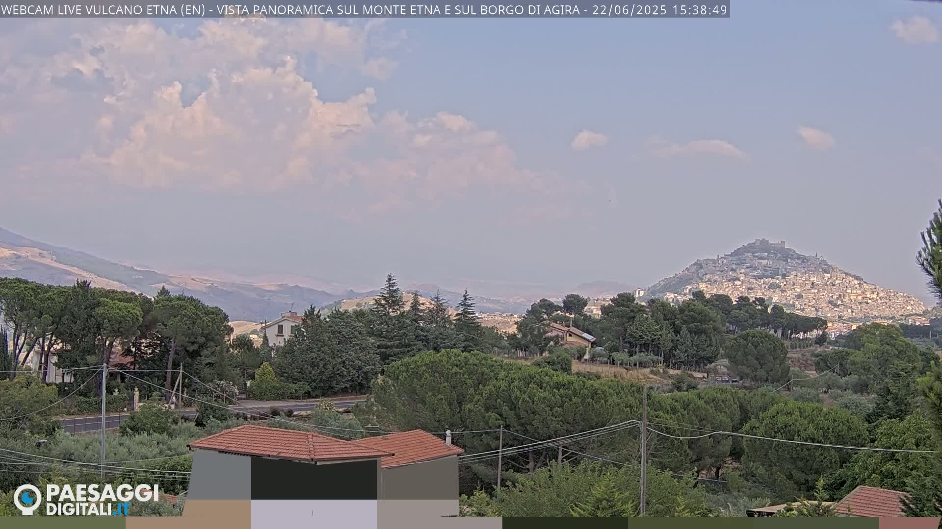 A partly cloudy day reveals a distant hilltop town nestled among rolling hills and lush green vegetation.