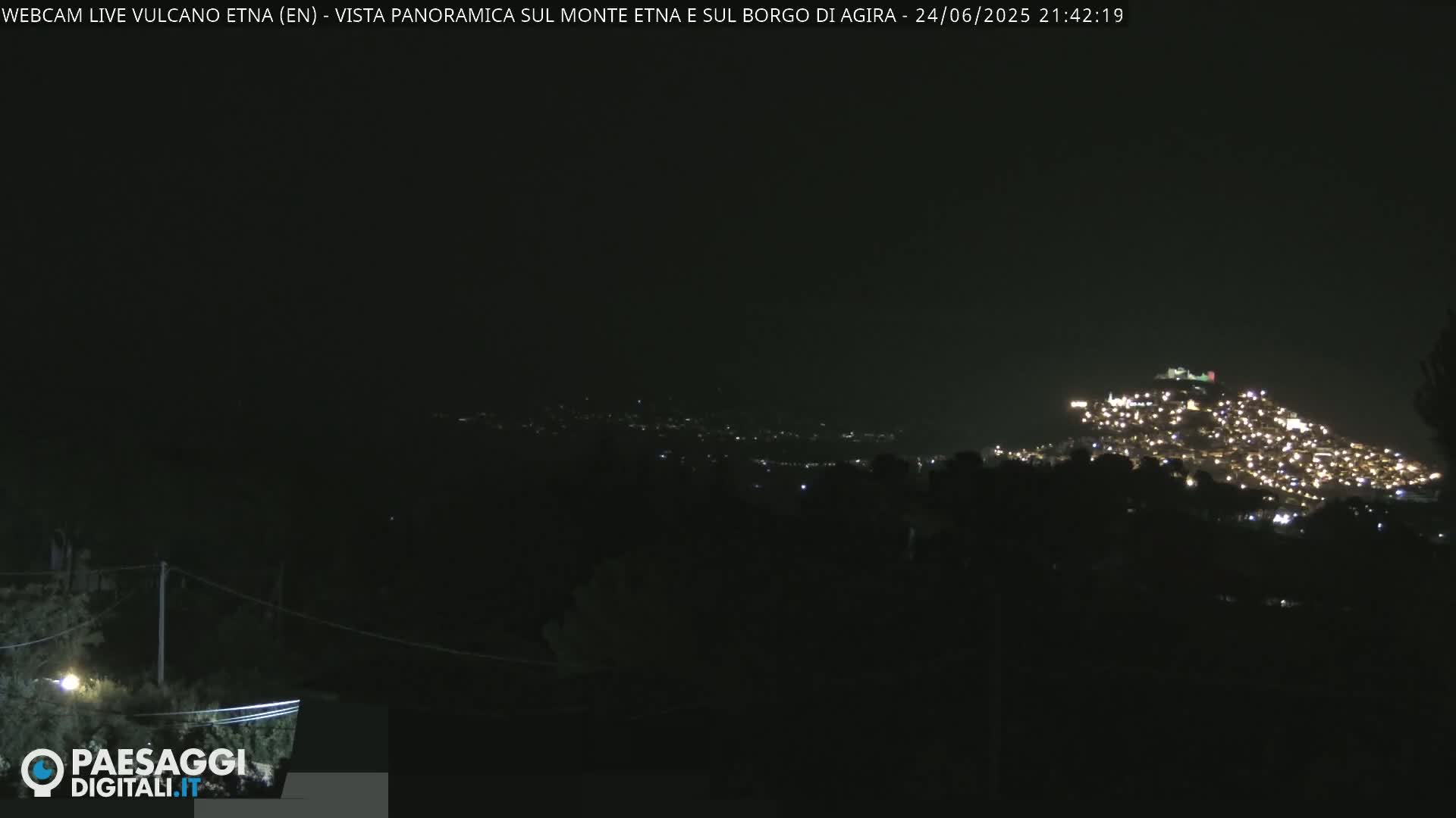 A nighttime view of a hilltop town illuminated with many lights, under a dark sky.