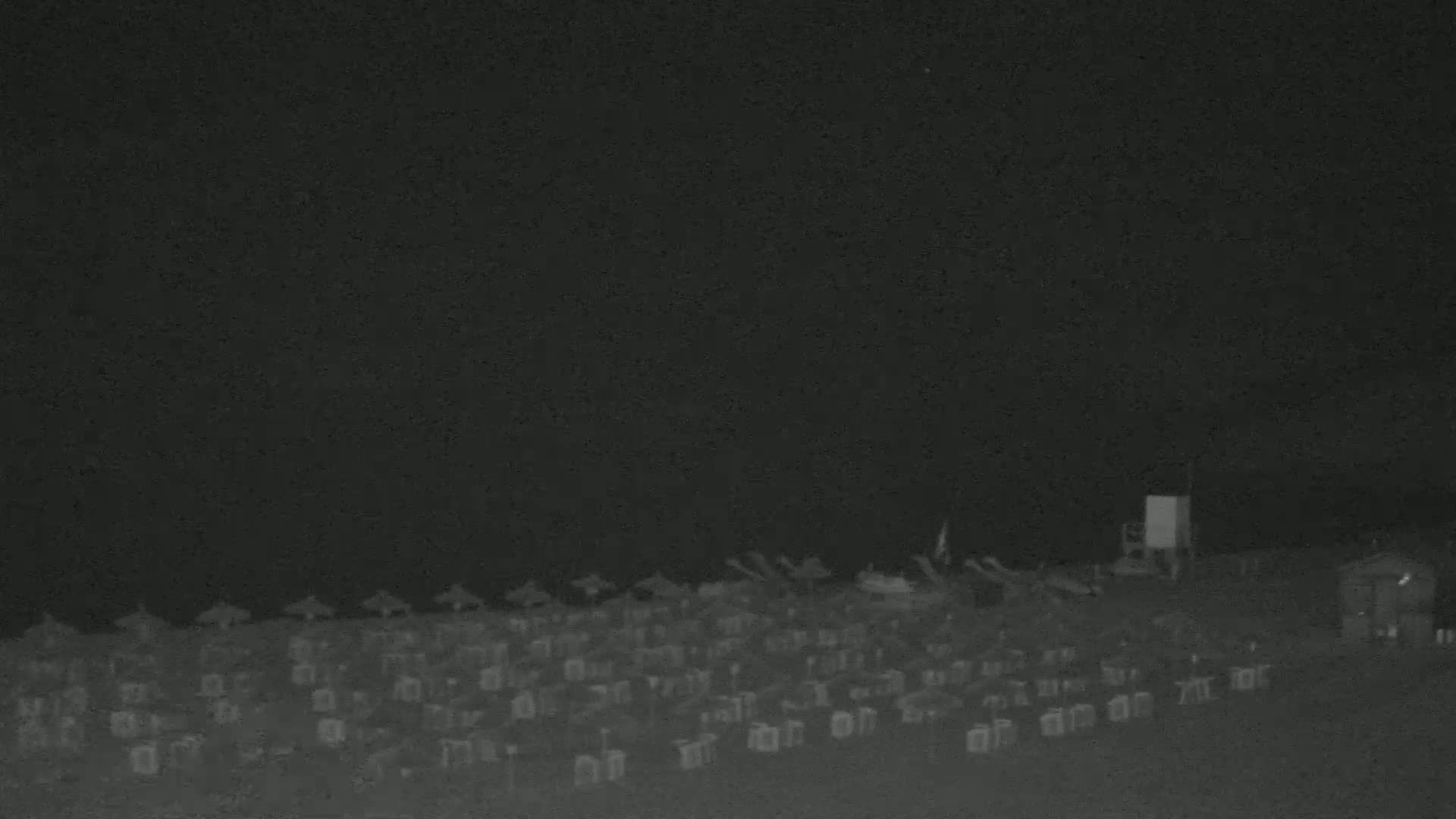 Under a dark night sky, numerous beach chairs and umbrellas are arranged on a beach.