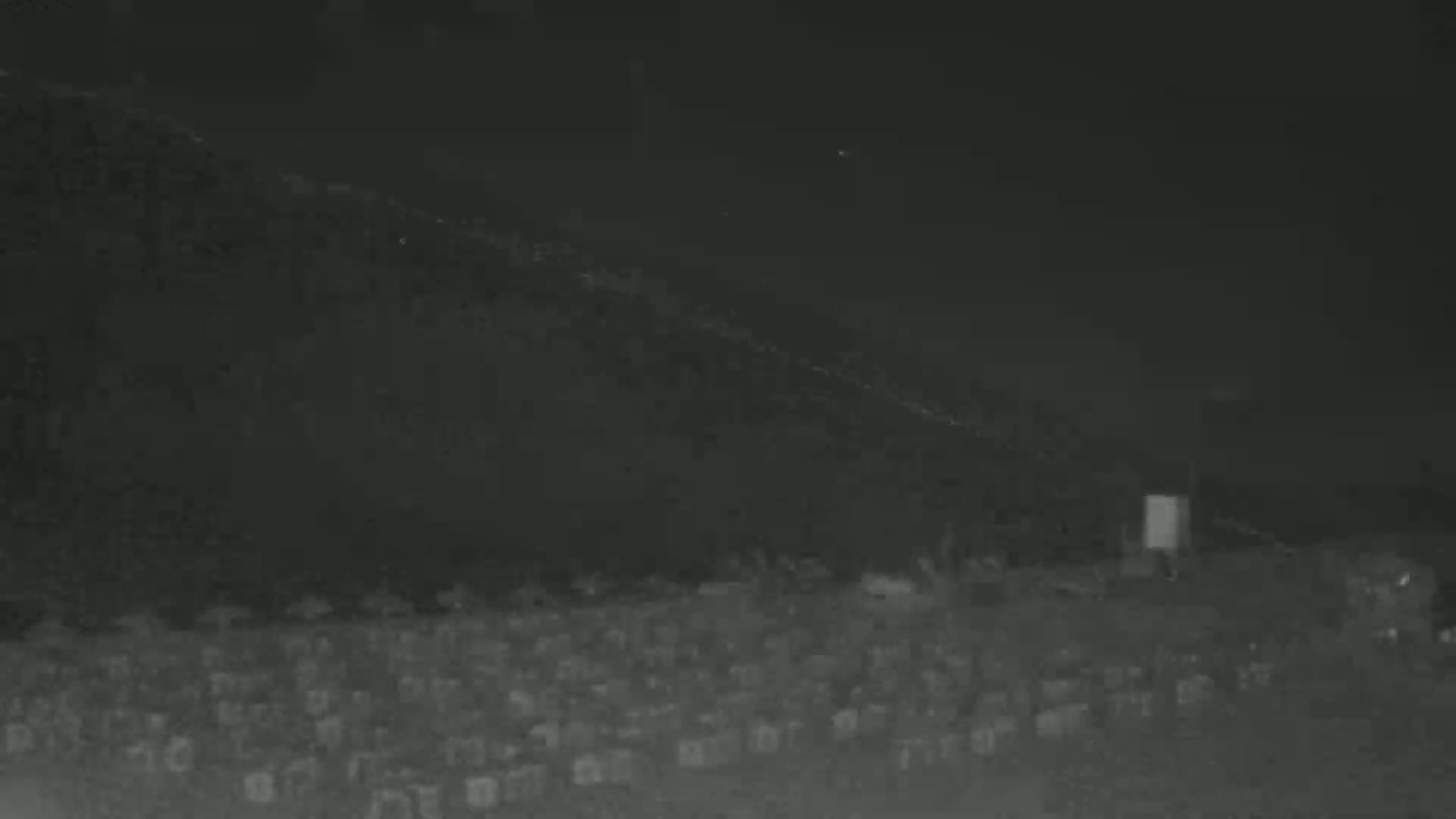 A nighttime, low-light image shows a large expanse of what appears to be a graveyard under a dark sky.