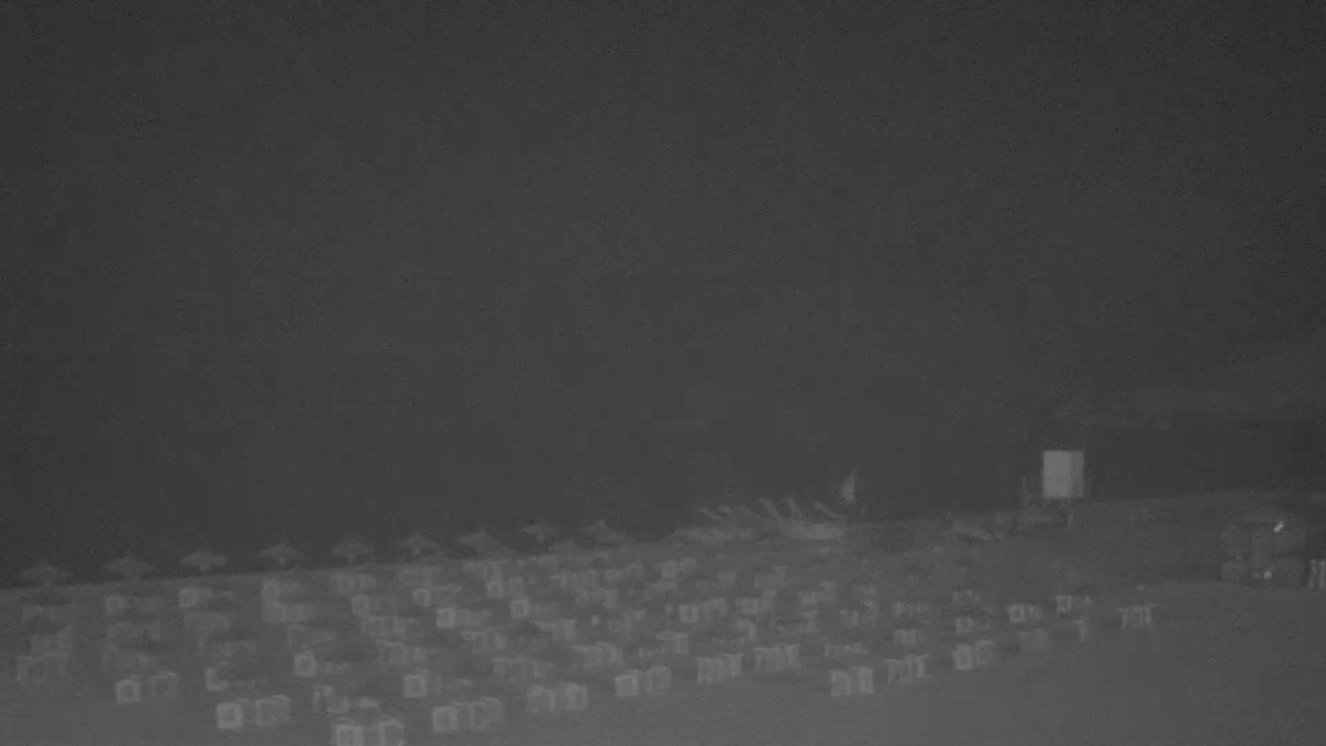 A nighttime, low-light view of numerous deck chairs arranged on a beach or similar outdoor space under a dark sky.