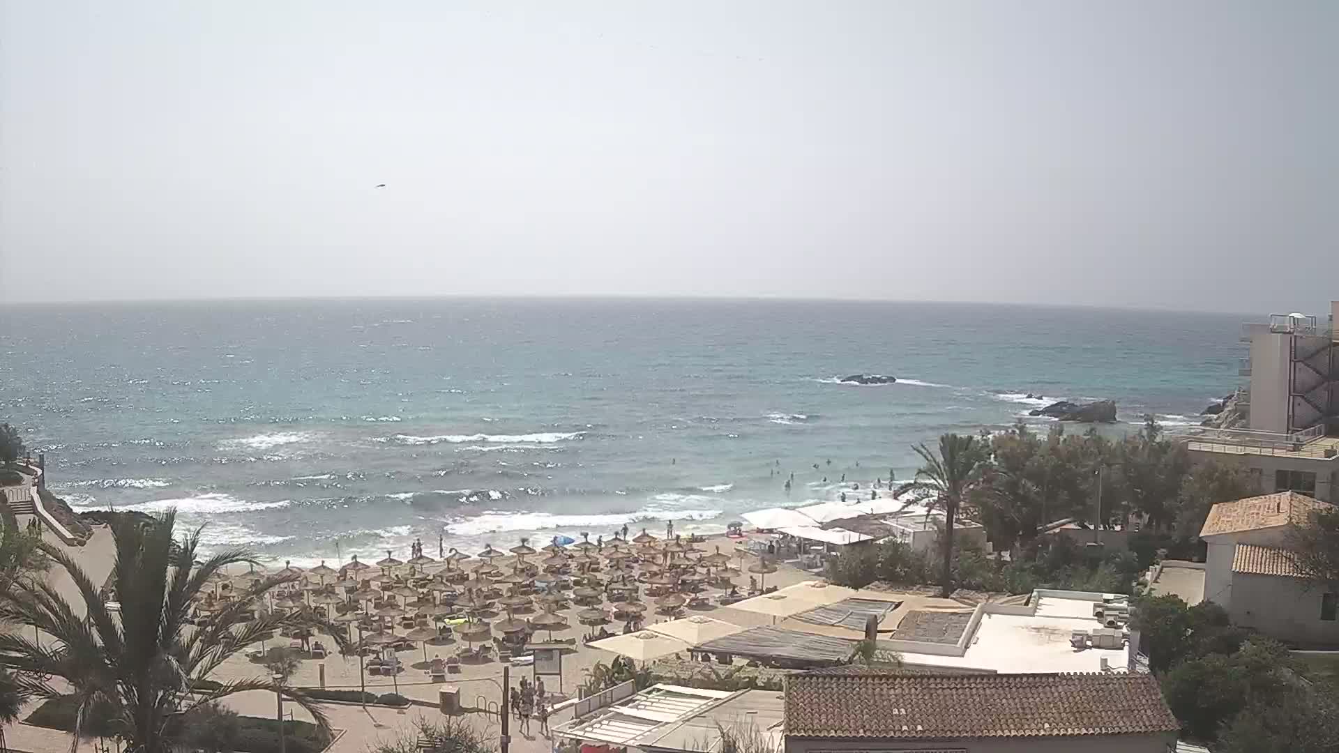 A beach with many umbrellas and people is visible, with a somewhat choppy sea under a hazy sky.