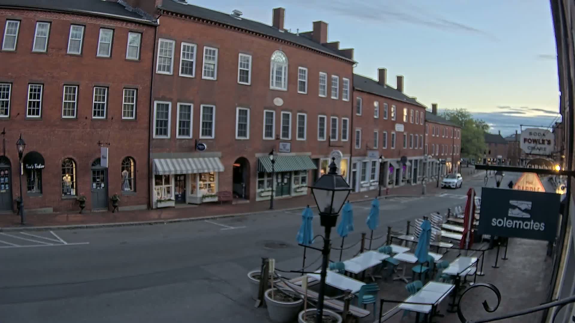 A mostly empty street lined with brick buildings and outdoor seating under a twilight sky.