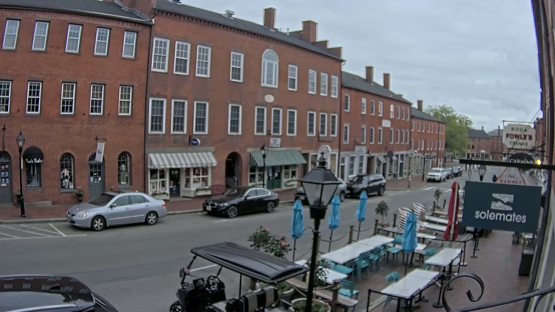 A street lined with brick buildings and outdoor seating under an overcast sky.