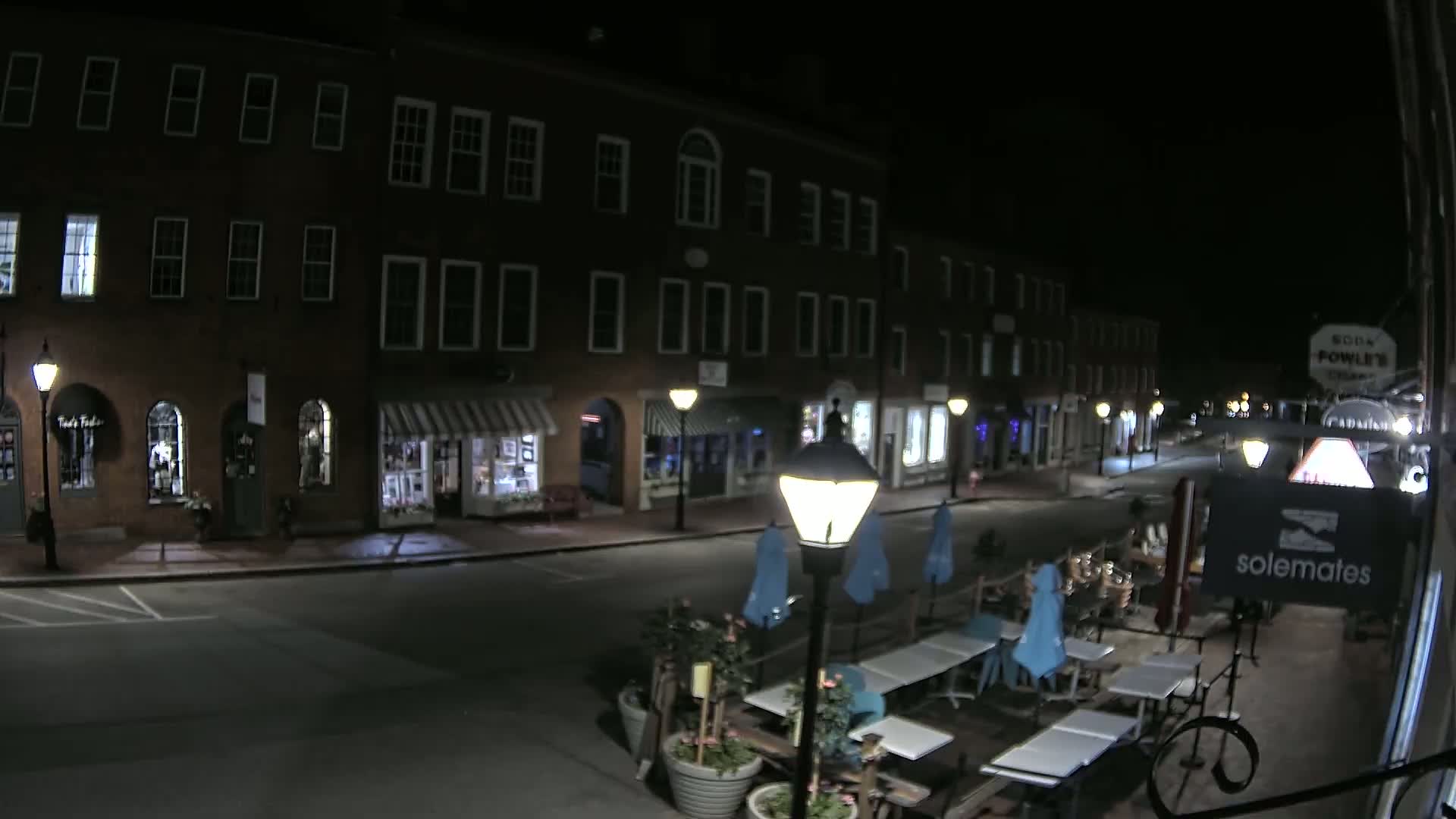 A nighttime street scene shows a row of brick buildings with shops and outdoor seating at a restaurant.