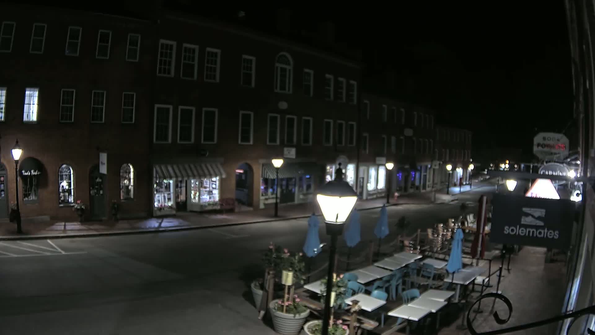 A nighttime view of a street lined with brick buildings and outdoor seating at a restaurant.