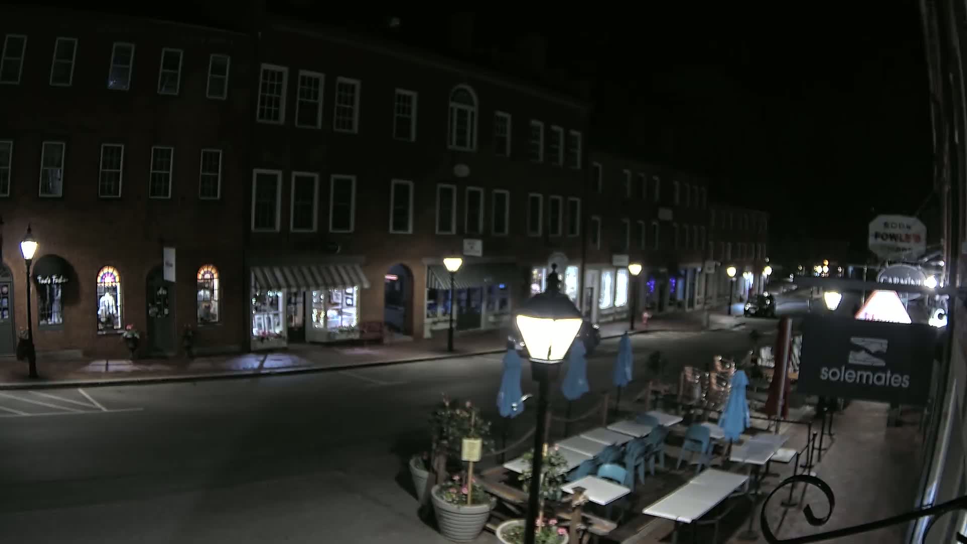 A nighttime street scene shows a row of brick buildings with shops and outdoor seating at a restaurant.