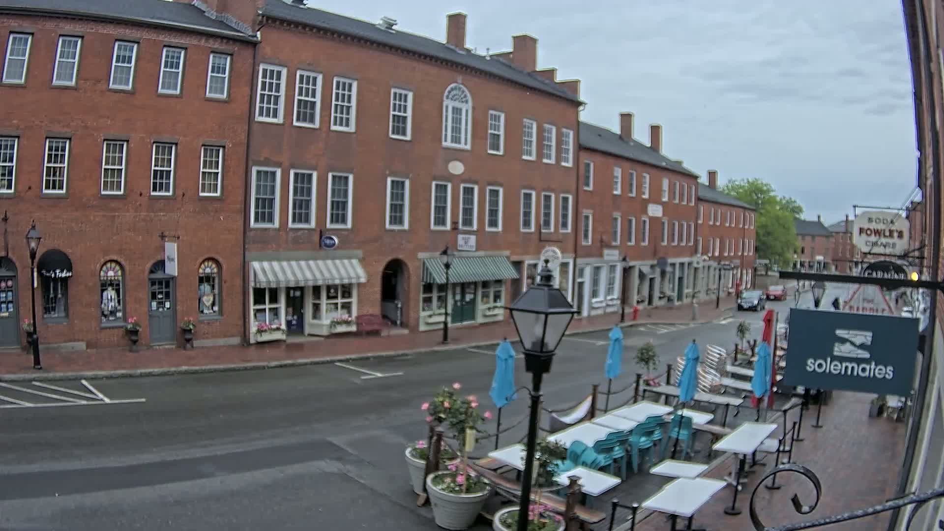 A brick street with shops and a restaurant patio is seen on an overcast day.