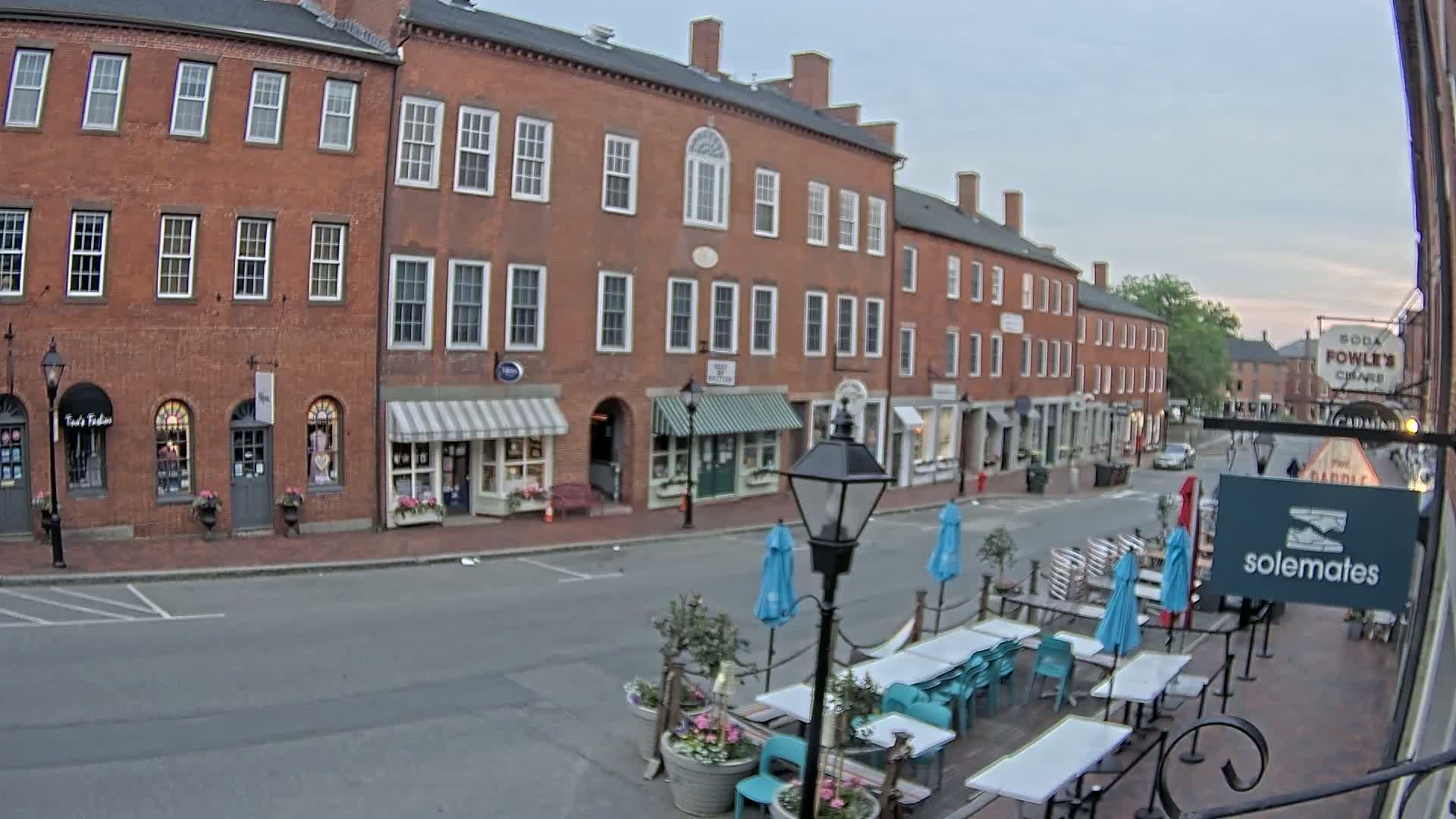A mostly empty street lined with brick buildings and outdoor seating areas under an overcast sky.