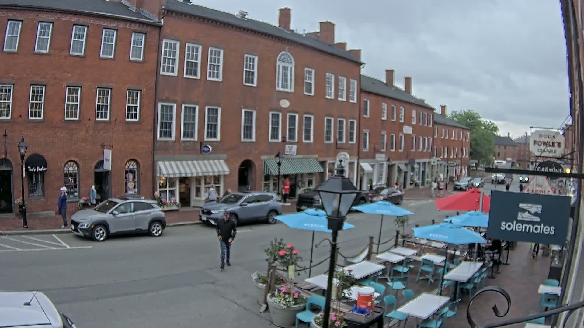 A rain-slicked street in front of several brick buildings with awnings and outdoor seating for a restaurant.
