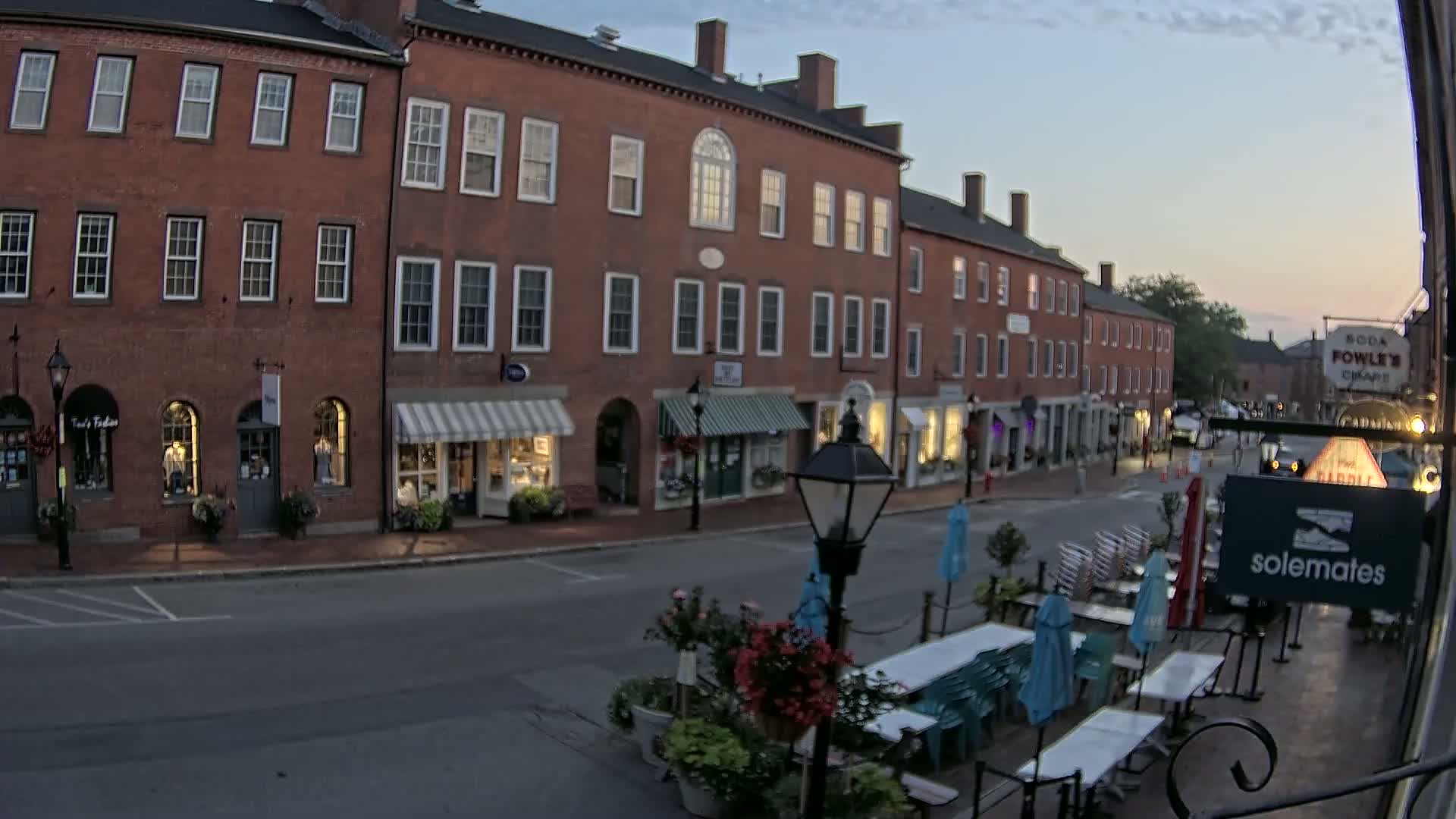 A nighttime street scene shows a row of brick buildings with shops and outdoor seating at a restaurant under a clear, dark sky.