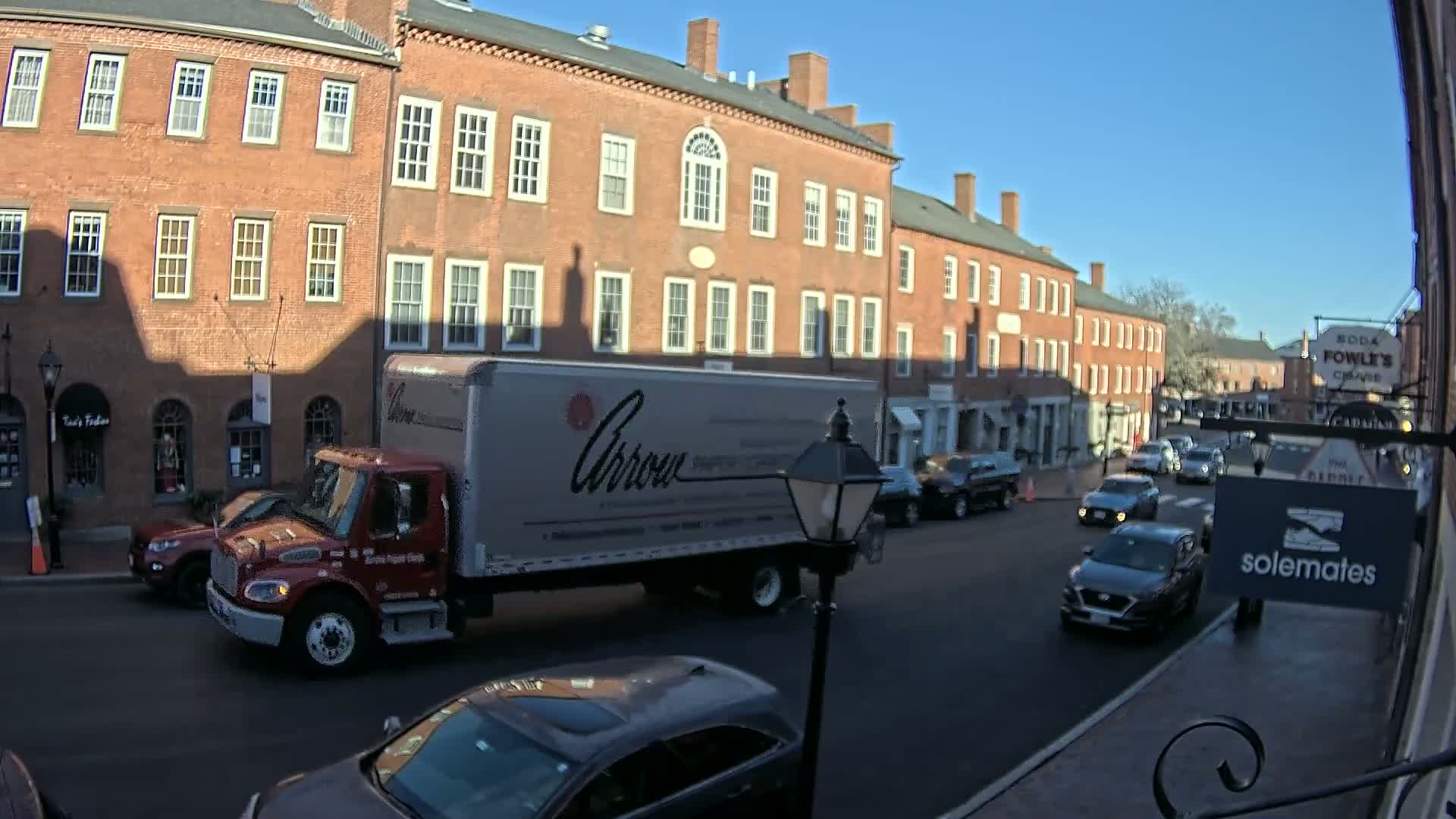 A nighttime street scene shows a row of brick buildings with shops and restaurants, some with outdoor seating, under a clear, dark sky.