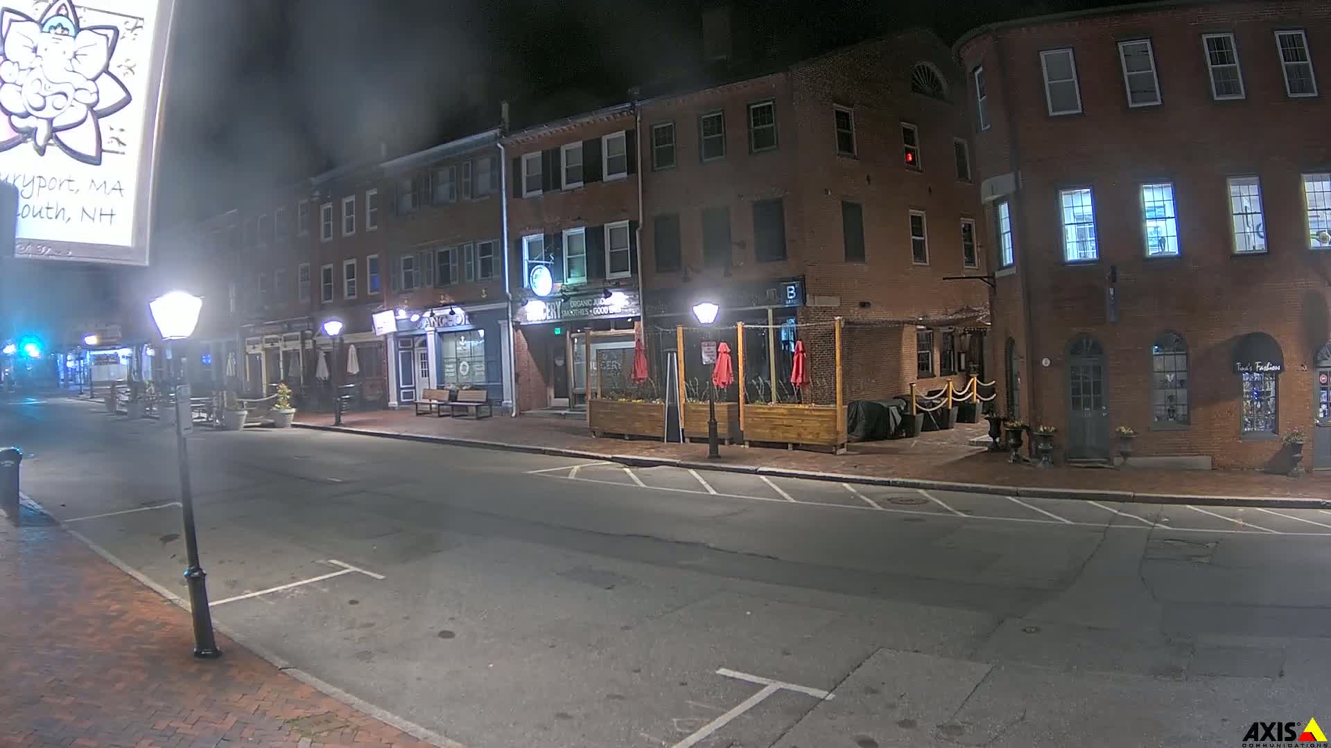 A mostly empty street at night lined with brick buildings, some with outdoor seating, under a slightly hazy sky.
