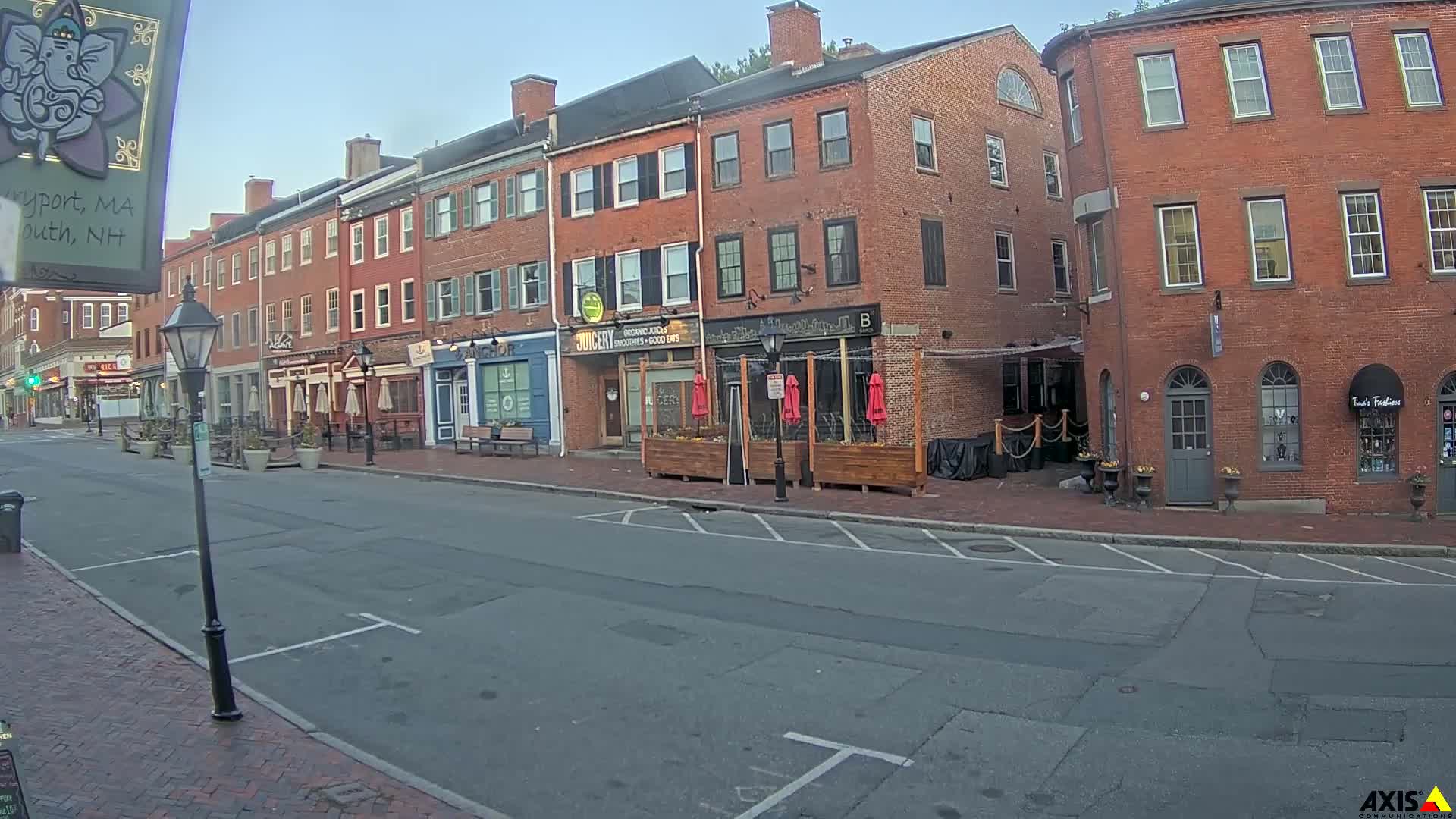 A mostly sunny street scene shows several brick buildings with outdoor seating areas in front of some businesses.