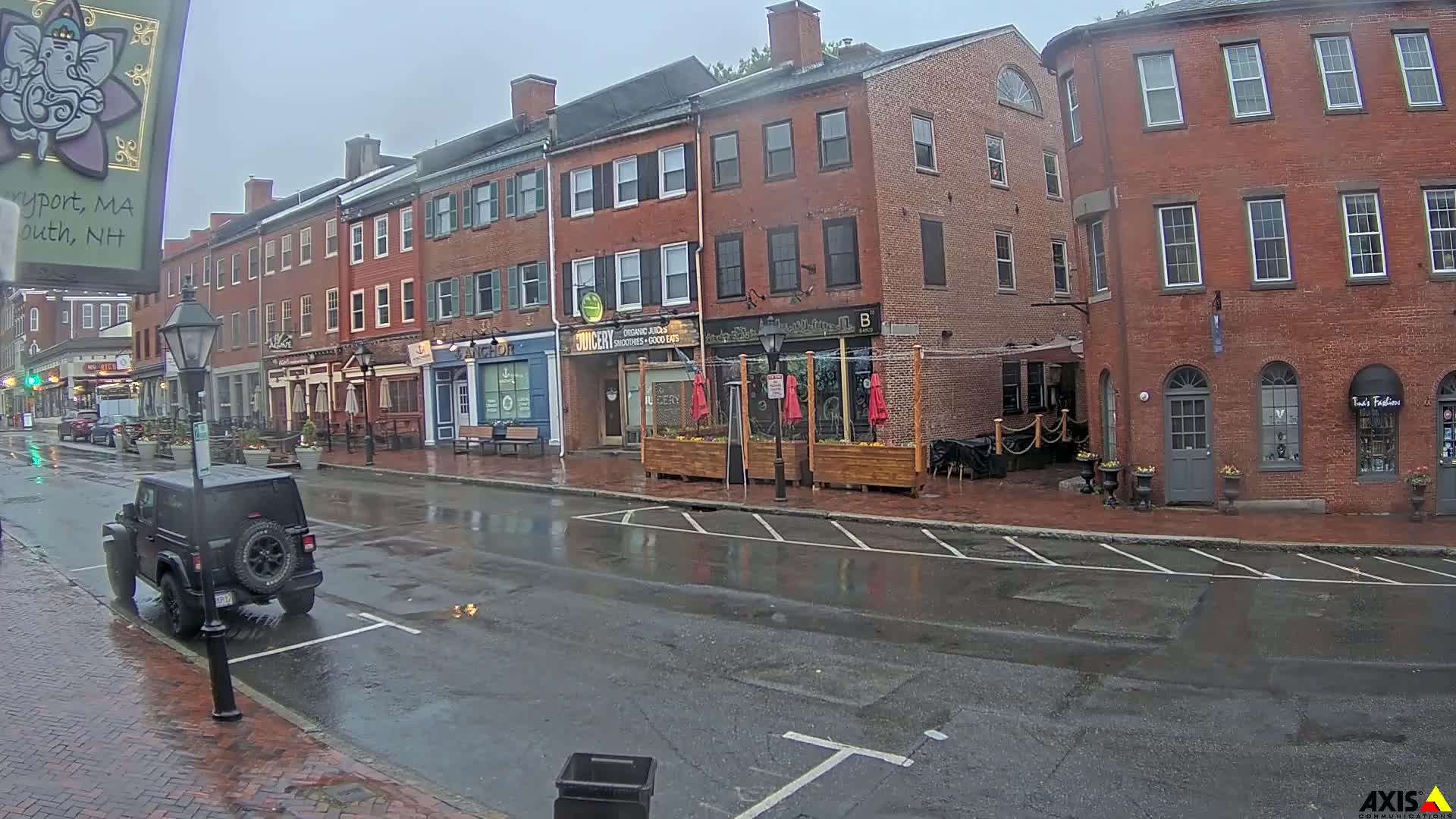 A rain-slicked street in front of several brick buildings with outdoor seating areas.