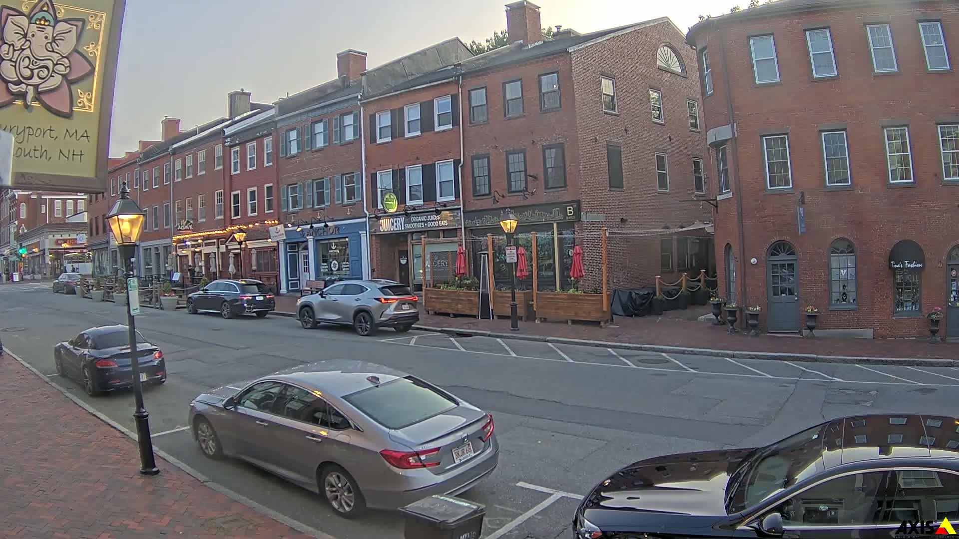 A city street lined with brick buildings and parked cars, under a twilight sky.