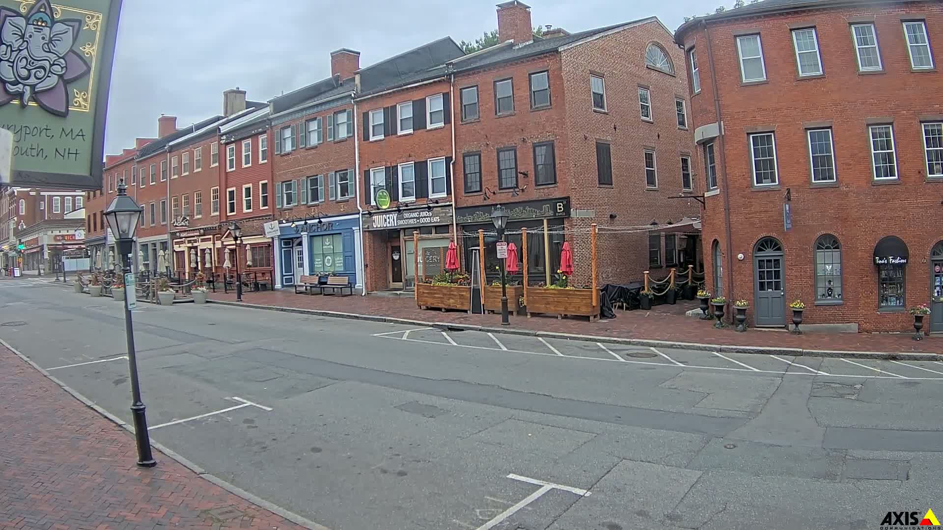 A brick-lined street with several shops and restaurants, under an overcast sky, features outdoor seating areas.