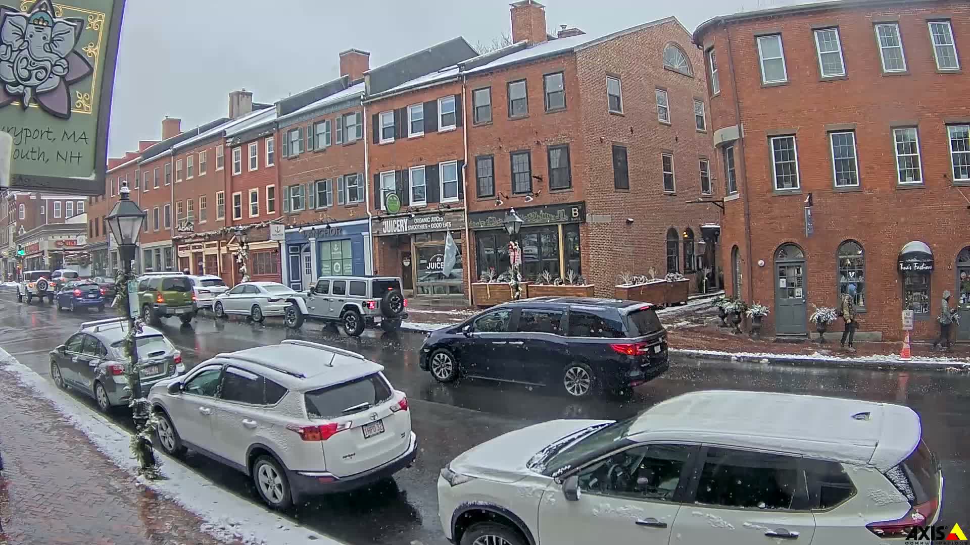 A nighttime view reveals a wet city street reflecting streetlights, flanked by historic brick buildings, with patches of snow remaining along the curbs.