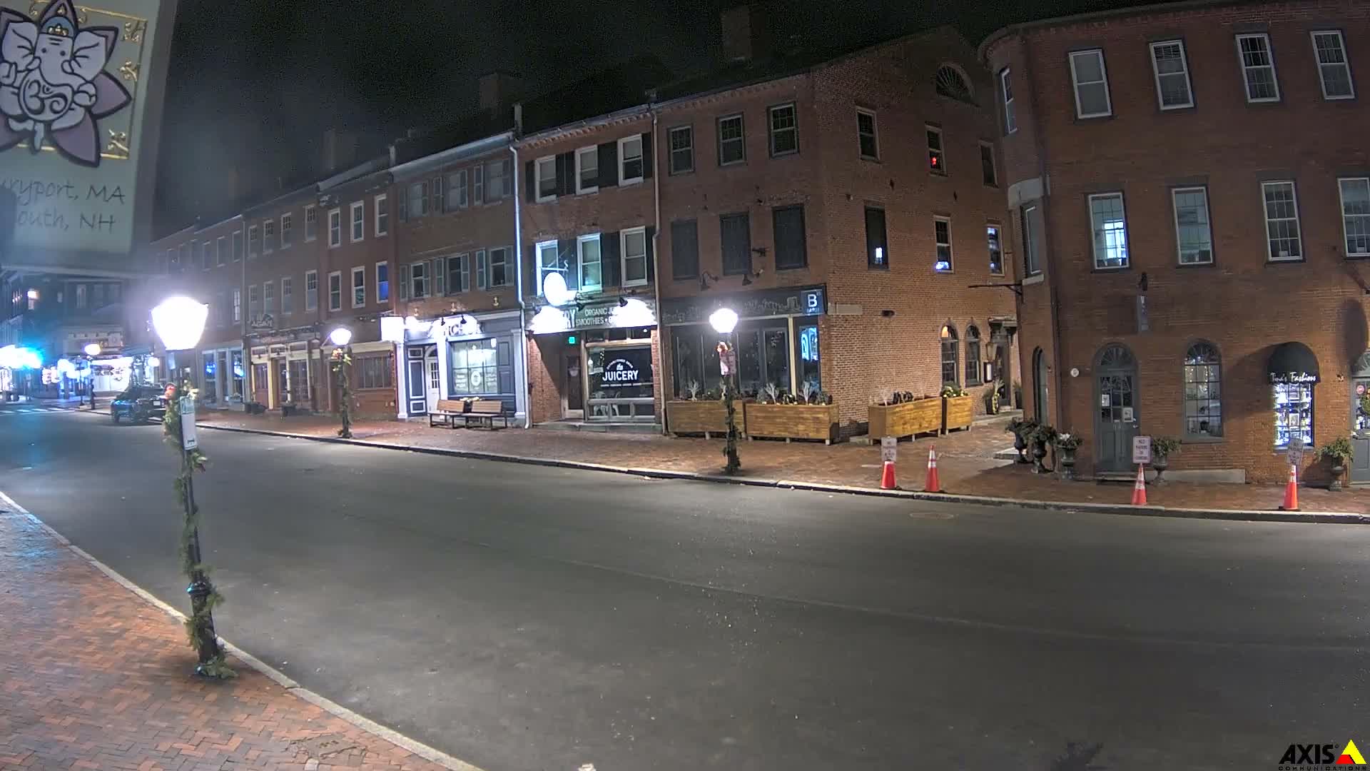 The image shows a quiet brick-lined street at night, illuminated by streetlights and shop windows, under clear skies.
