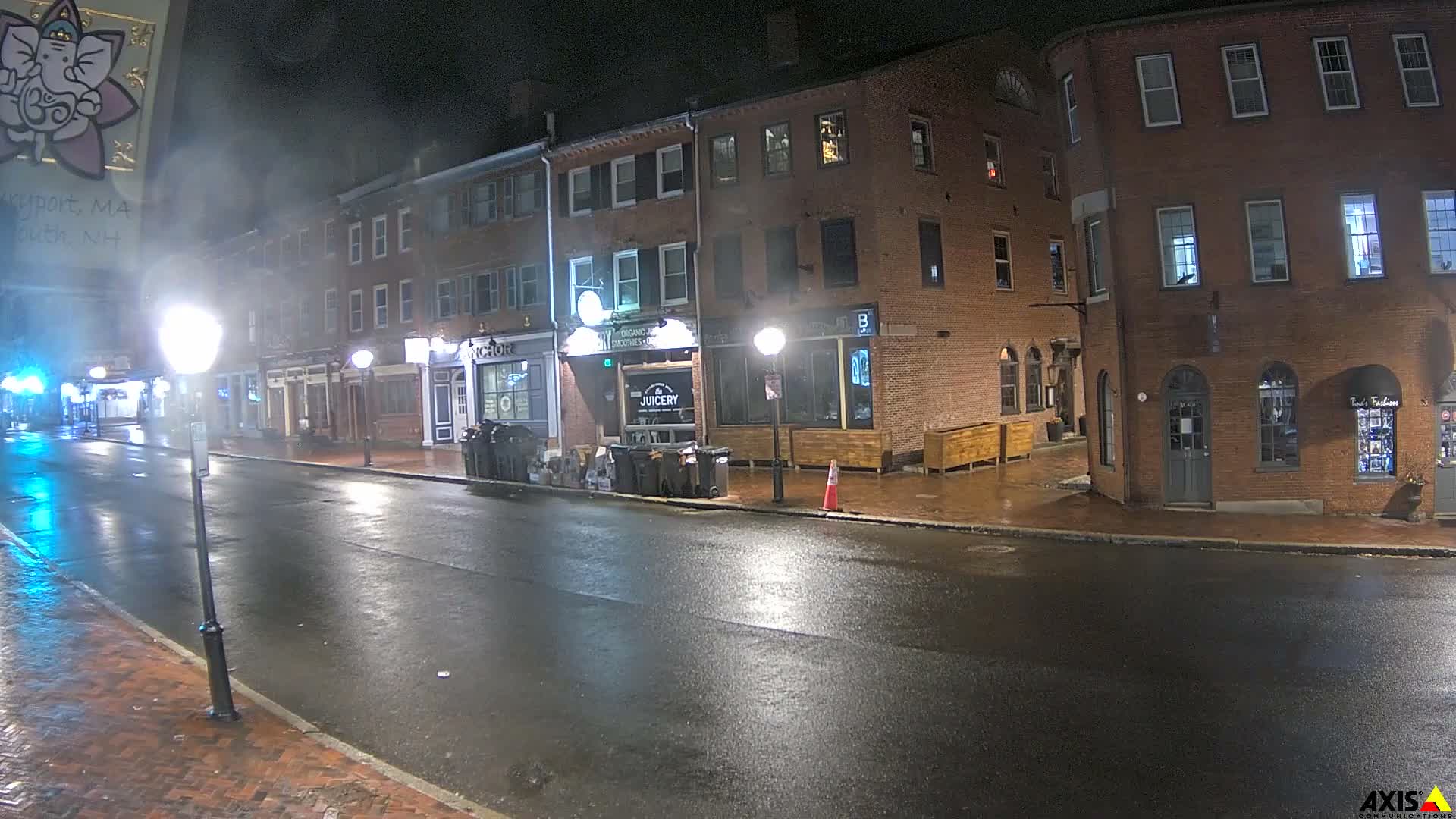 The image shows a quiet brick-lined street at night, illuminated by streetlights and shop windows, under clear skies.