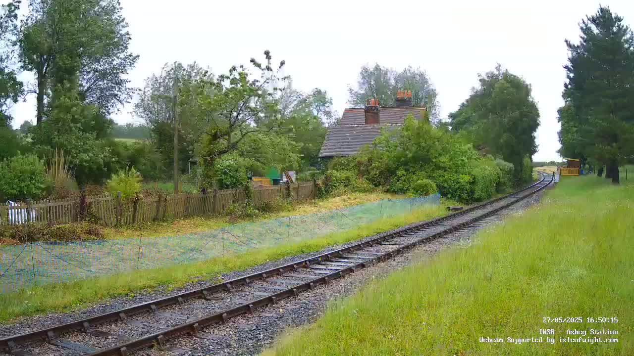 A railway track extends into the distance past a small house and wooden fence, under an overcast sky.