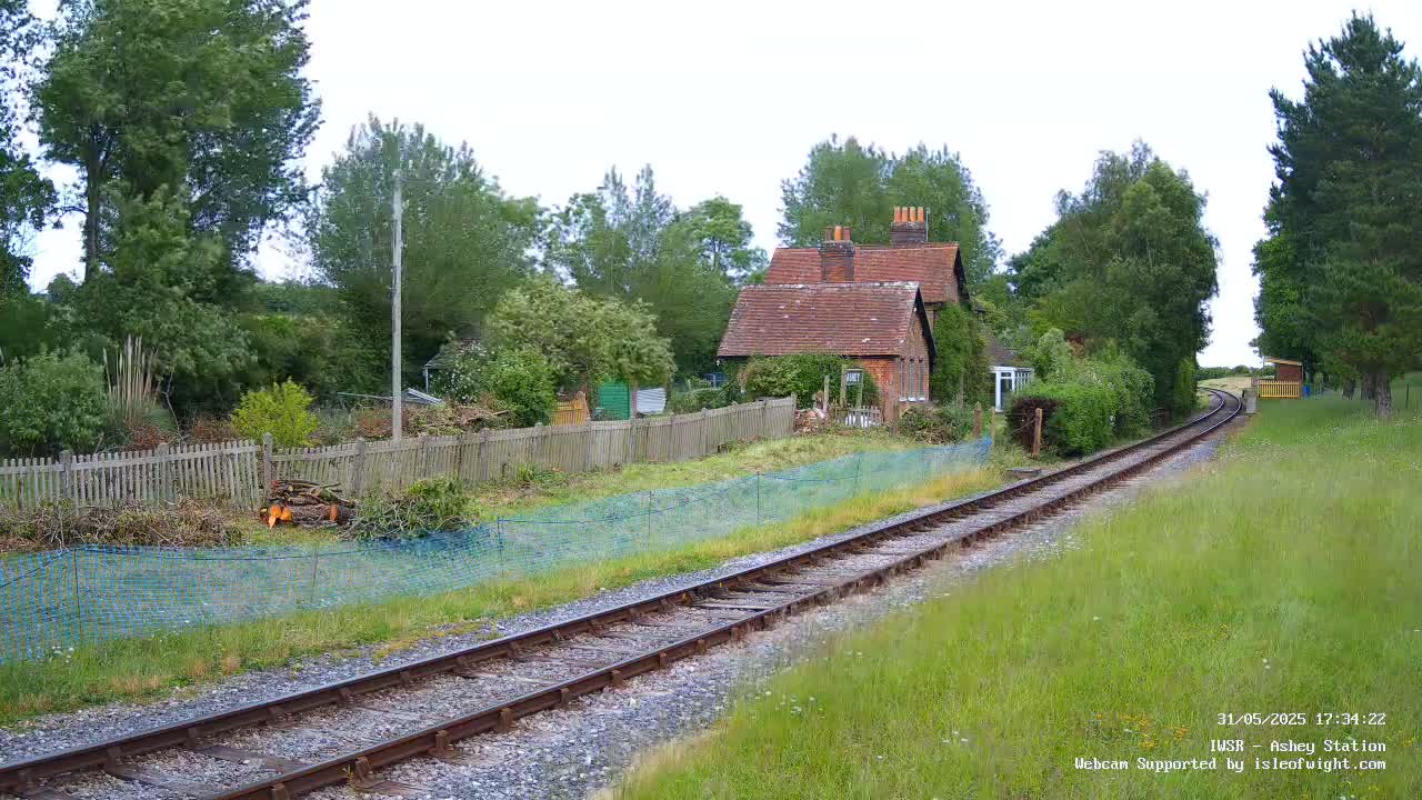 A brick house sits behind a wooden fence next to a railway track on an overcast day.