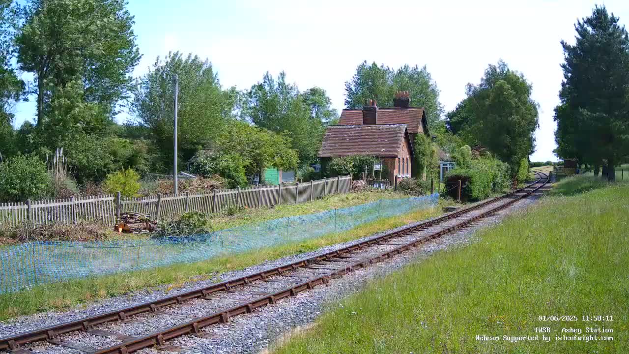 A brick building sits behind a wooden fence next to a railway track on a sunny day.