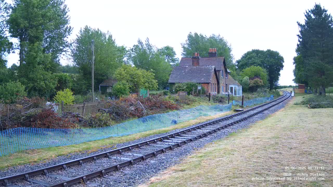 A railway track extends from a small house toward a cluster of trees under an overcast sky.