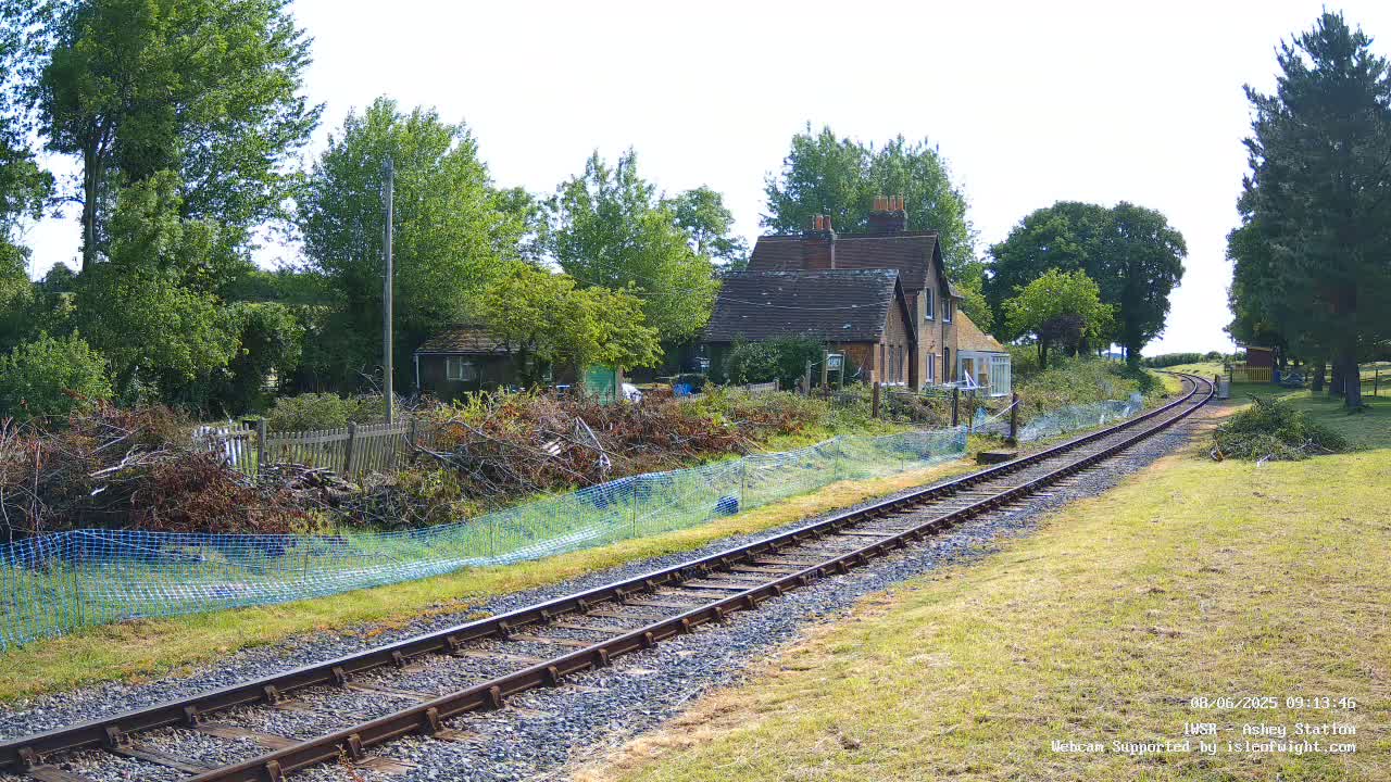 A railway track extends into the distance past a house and several trees on a sunny day.