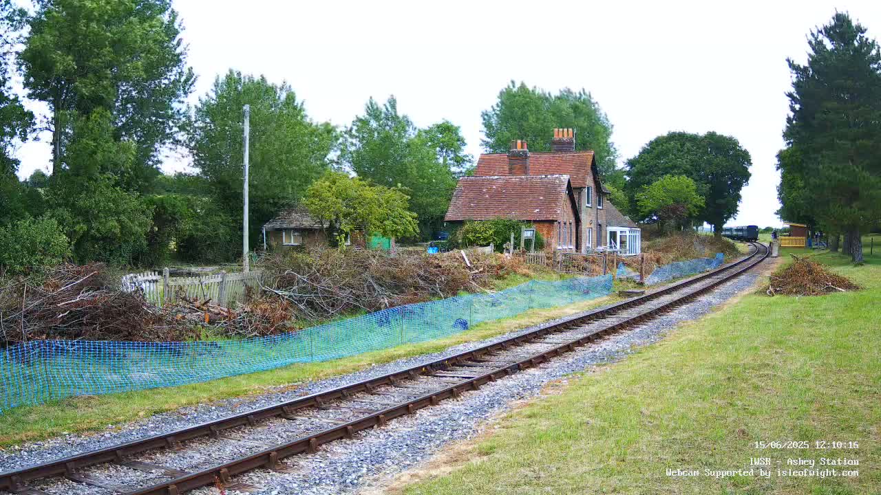 A train is seen in the distance approaching a small house next to a railway track on an overcast day.