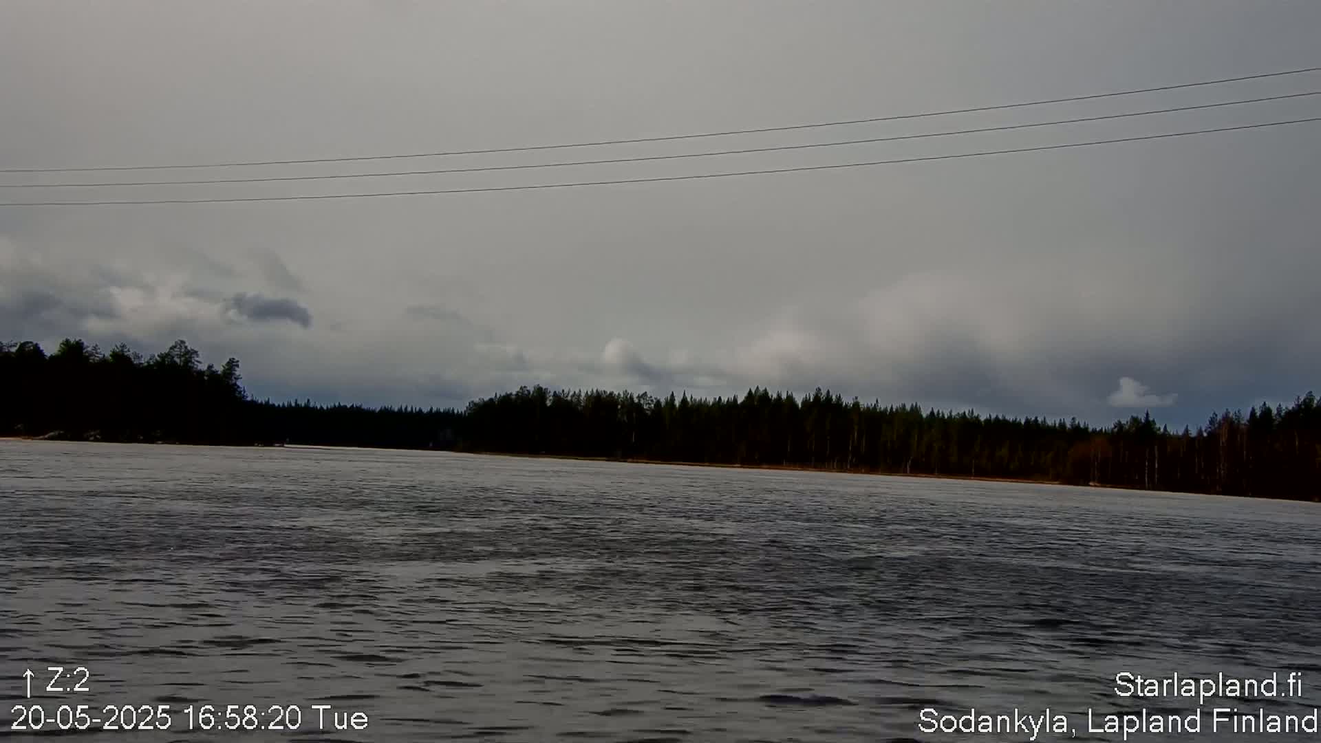 A wide, dark river flows under an overcast sky, toward a treeline in the distance.