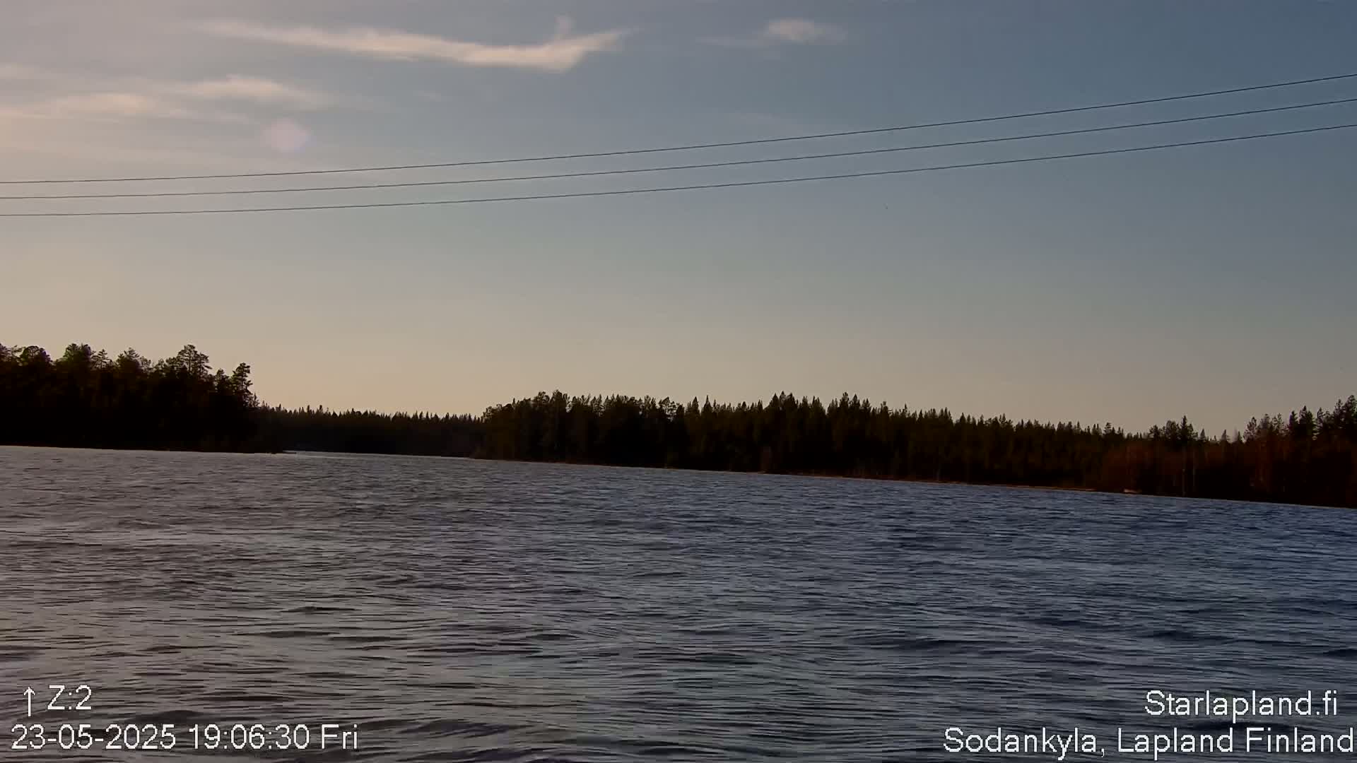 Under a partly cloudy sky, a calm body of water stretches out before a dark line of trees.
