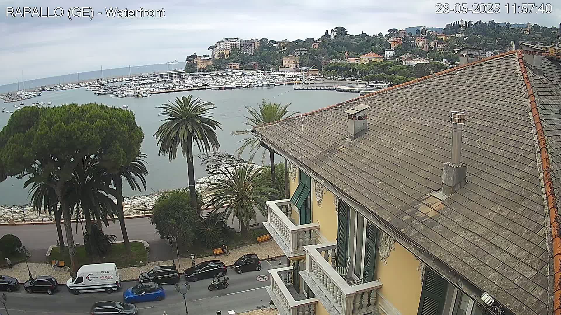 A waterfront view of a harbor filled with boats, overlooked by a multi-story building with a tiled roof, under an overcast sky.