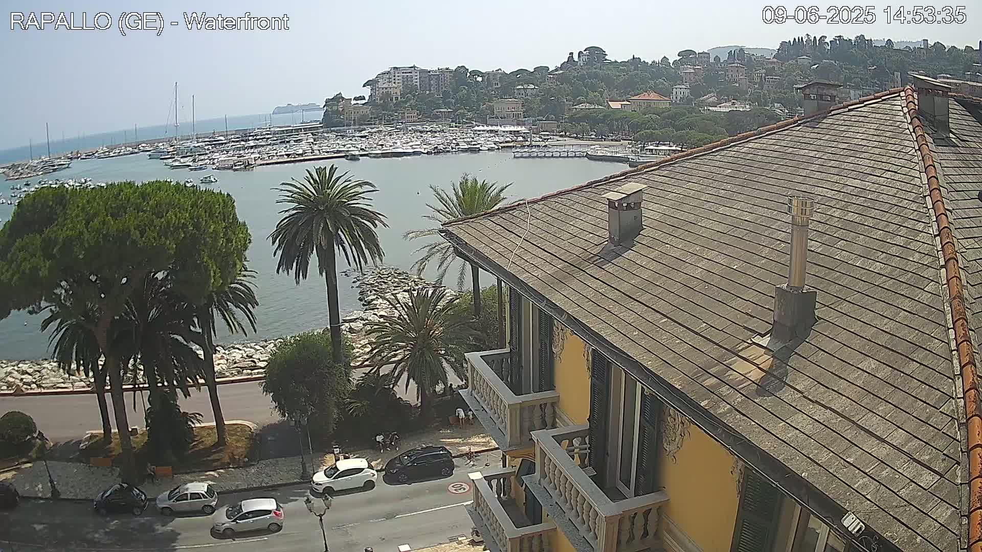 A seaside town with a harbor full of boats is viewed from a yellow building's rooftop on a sunny day.