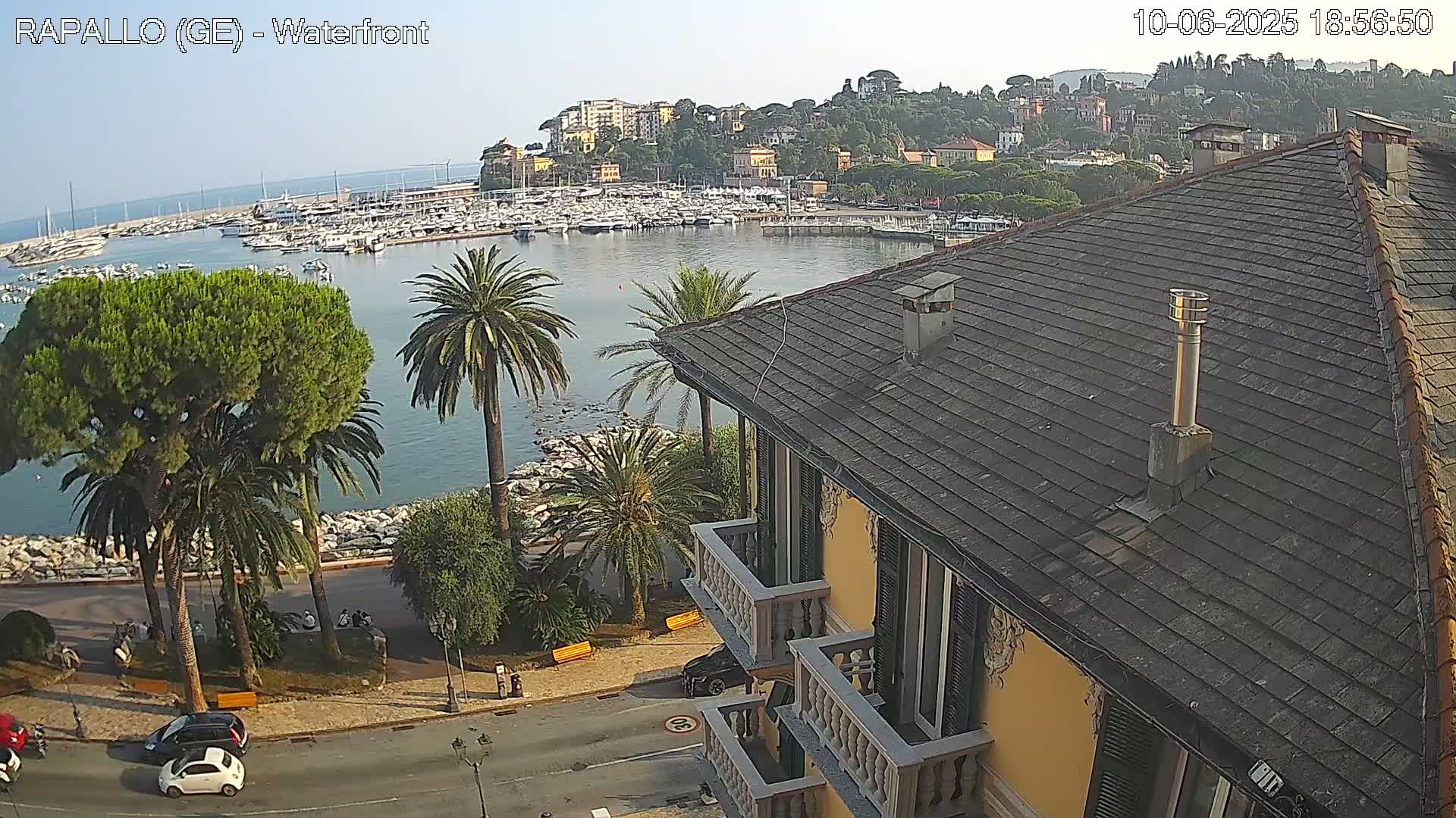 A view from a building overlooking a harbor filled with boats, a waterfront road, and a hillside town under a clear sky.
