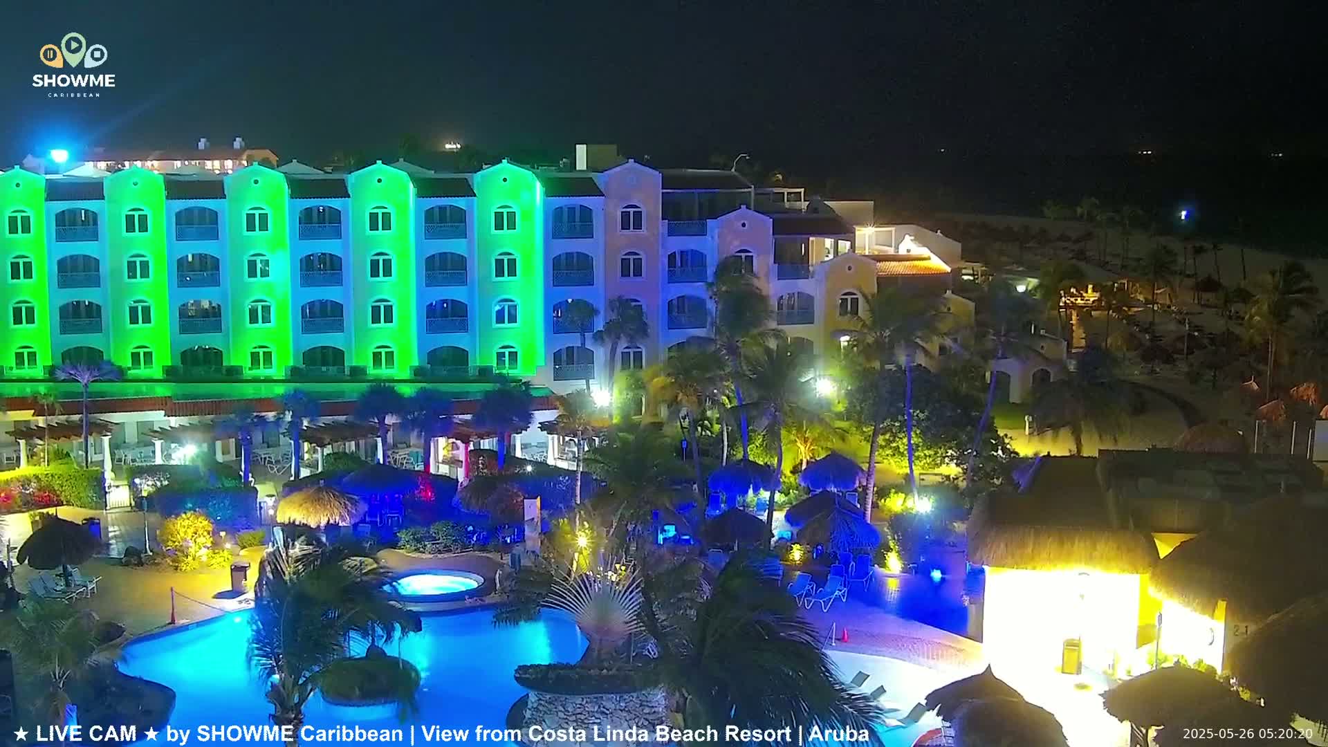 A brightly lit resort at night, featuring a large pool and a multi-story building with green and blue lighting, is shown under a dark sky.