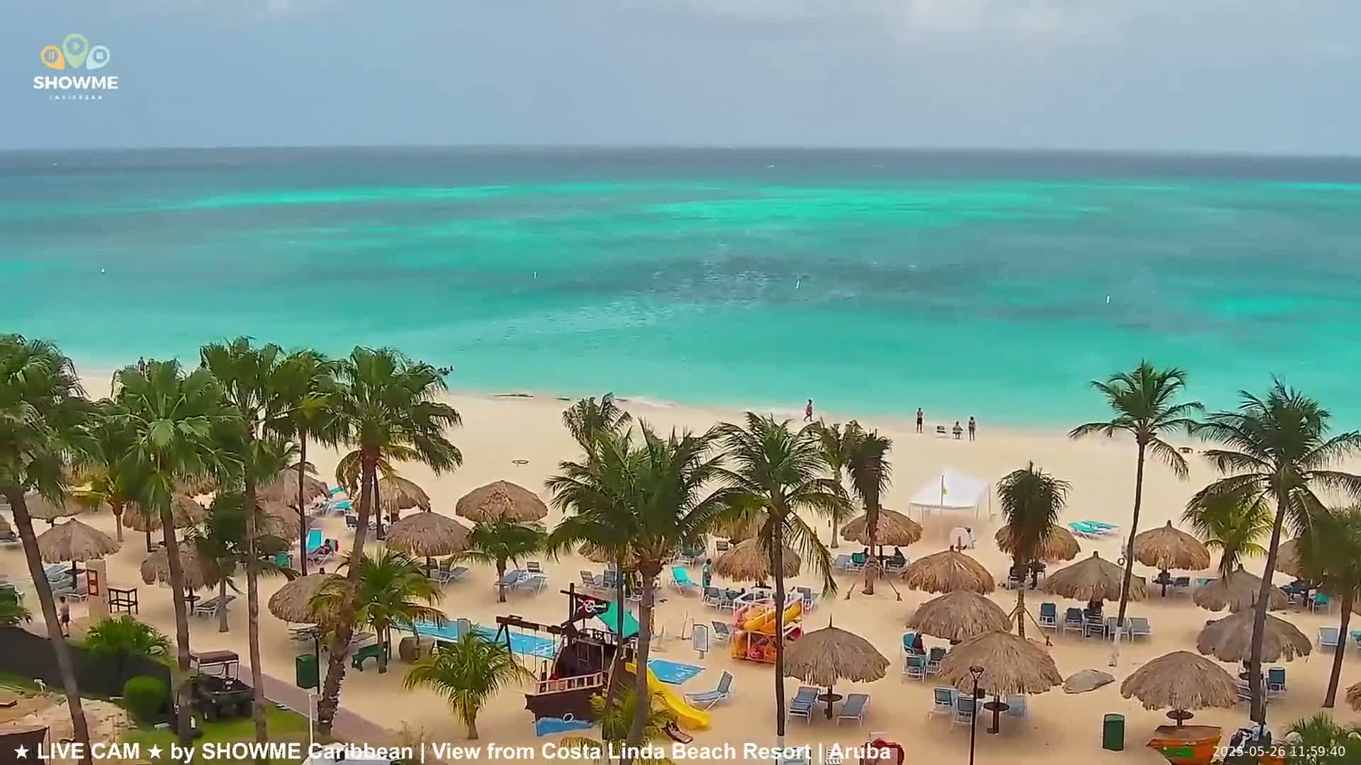 A beach with turquoise water, palm trees, and thatched umbrellas under an overcast sky.